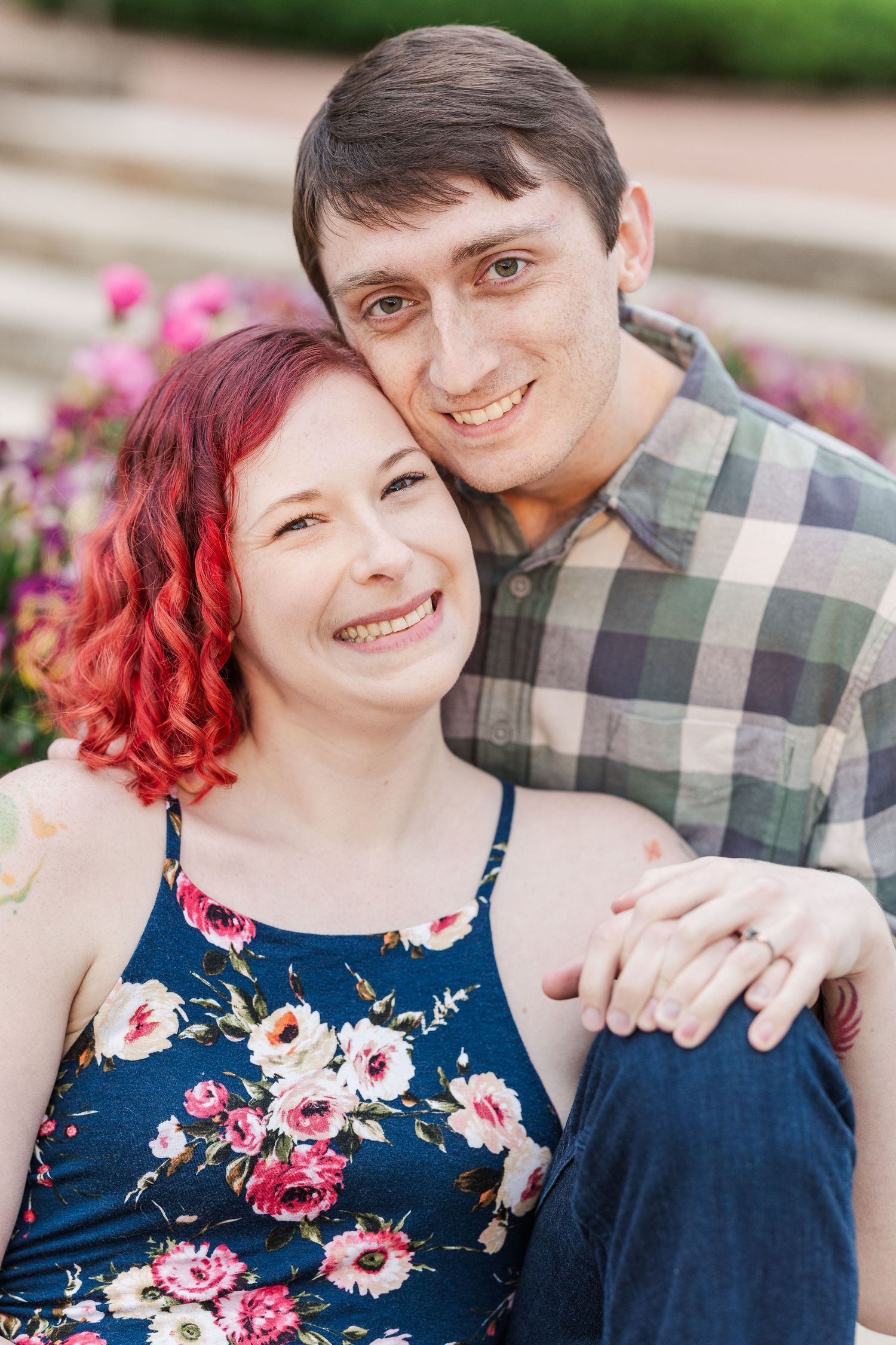 A couple embraces outdoors, with one person wearing a plaid shirt and the other in a floral navy dress with bright red curly hair at Cantign