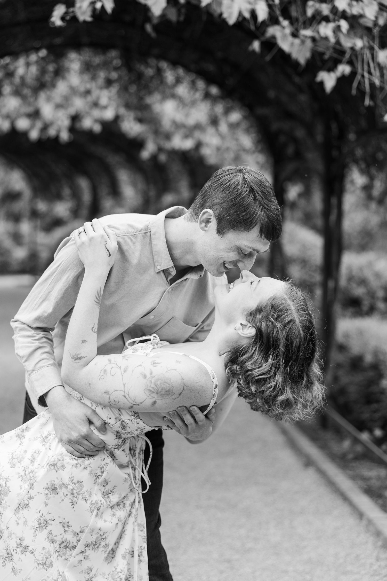 A romantic black and white photo of a couple embracing in a dip pose under tree branches in a garden setting at Cantigny Park
