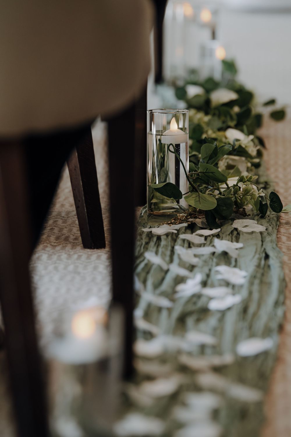 Glass vase with eucalyptus leaves and floral table decor arrangement reflecting on mirrored surface.