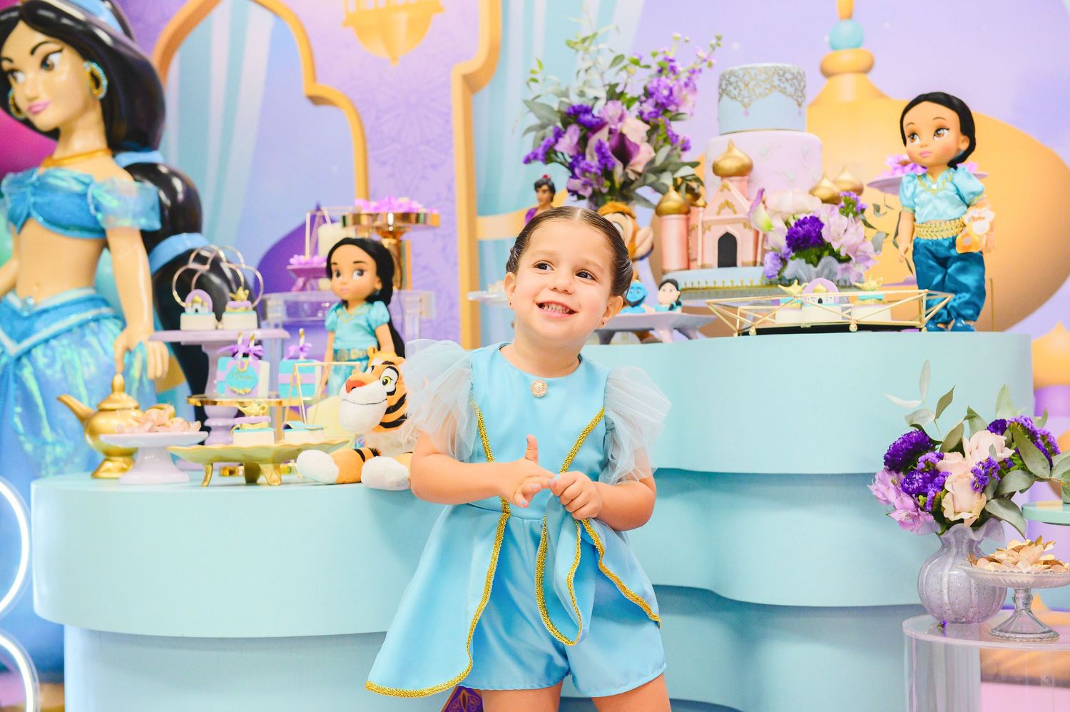 A colorful princess-themed birthday party setup with blue and purple decor, tiered display stands, and floral arrangements.
