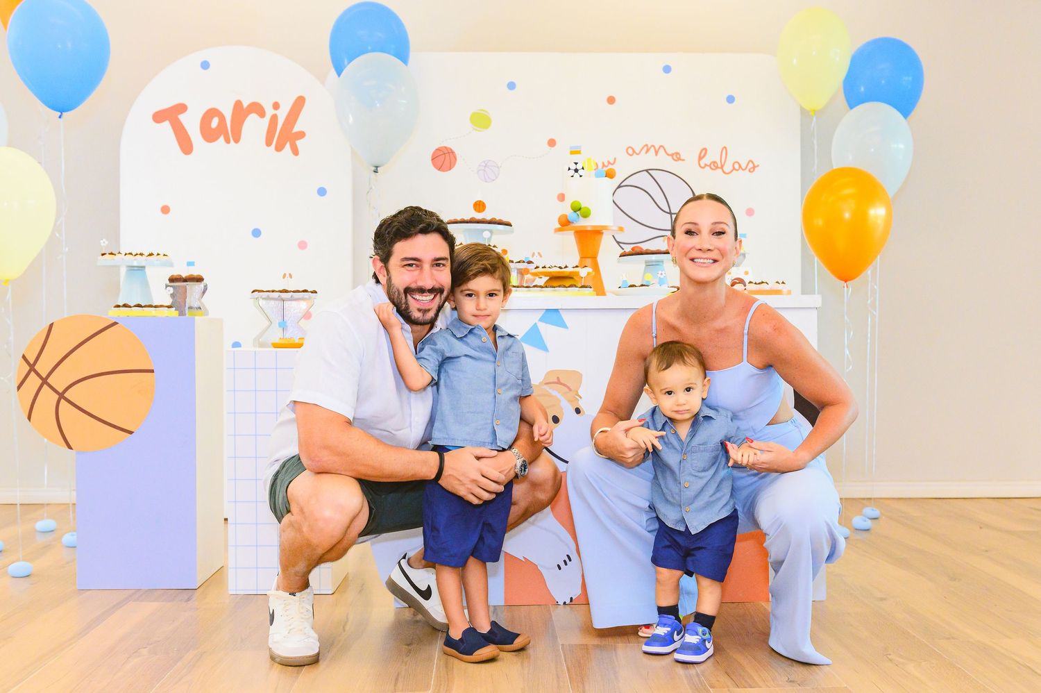 A family poses together at a child's birthday party with blue balloons and basketball decor in a bright room.