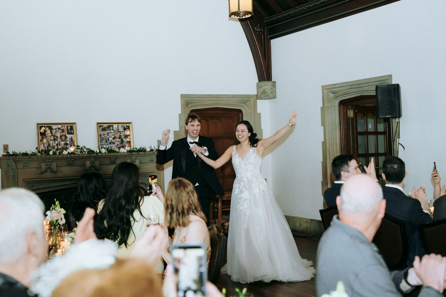 Wedding reception celebration with guests cheering in historic interior venue.
