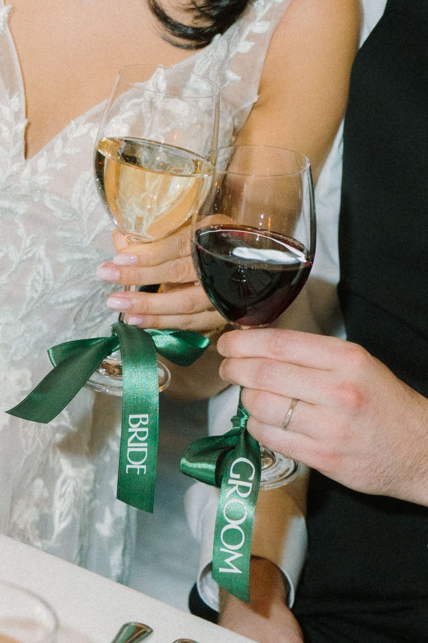Wedding toast with red and white wine glasses adorned with green ribbons.