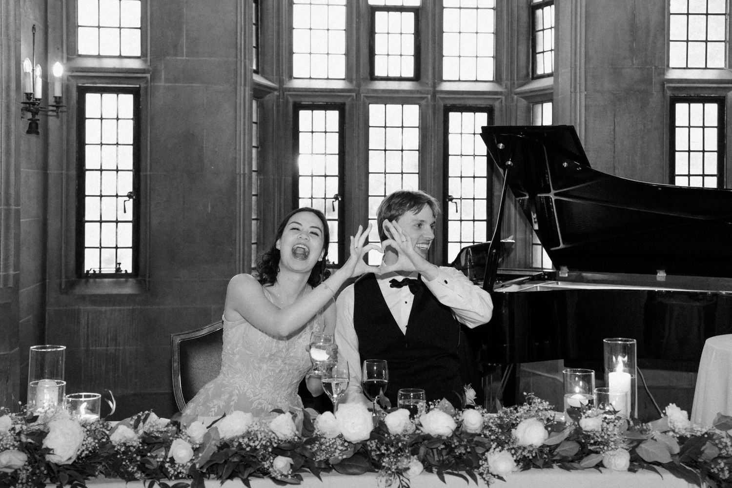 A wedding celebration by a grand piano with elegant floral arrangements at a formal reception venue.