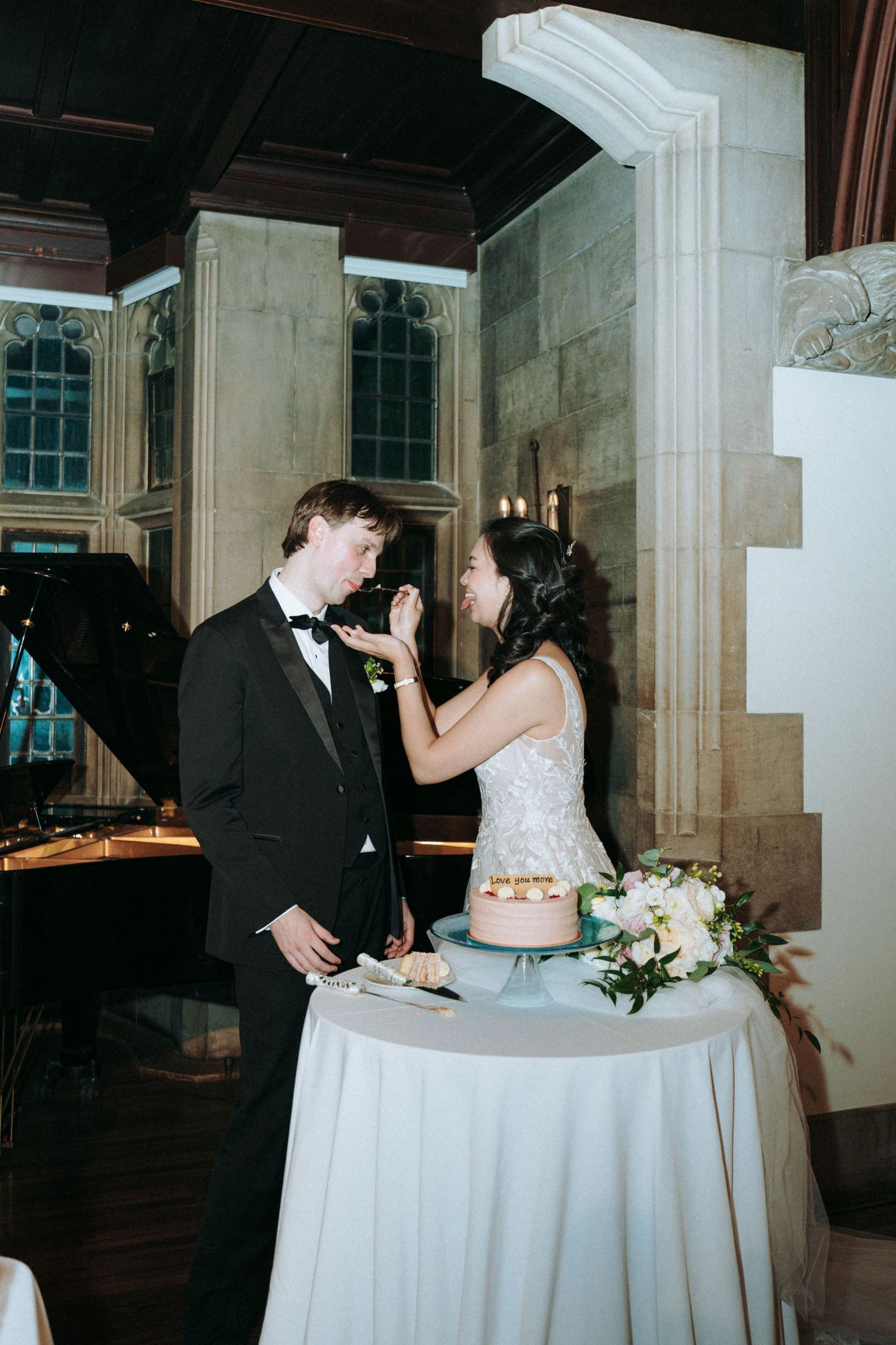 A couple sharing cake at their wedding reception beside an elegant floral centerpiece.
