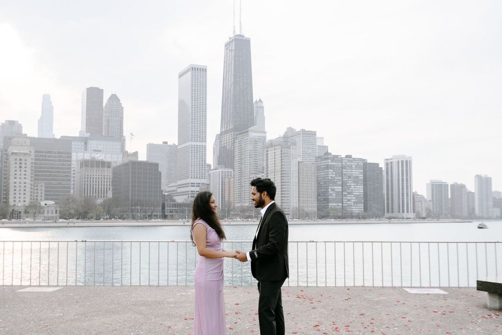 A couple shares a romantic moment at the waterfront with the Chicago skyline visible in the background on a misty day.