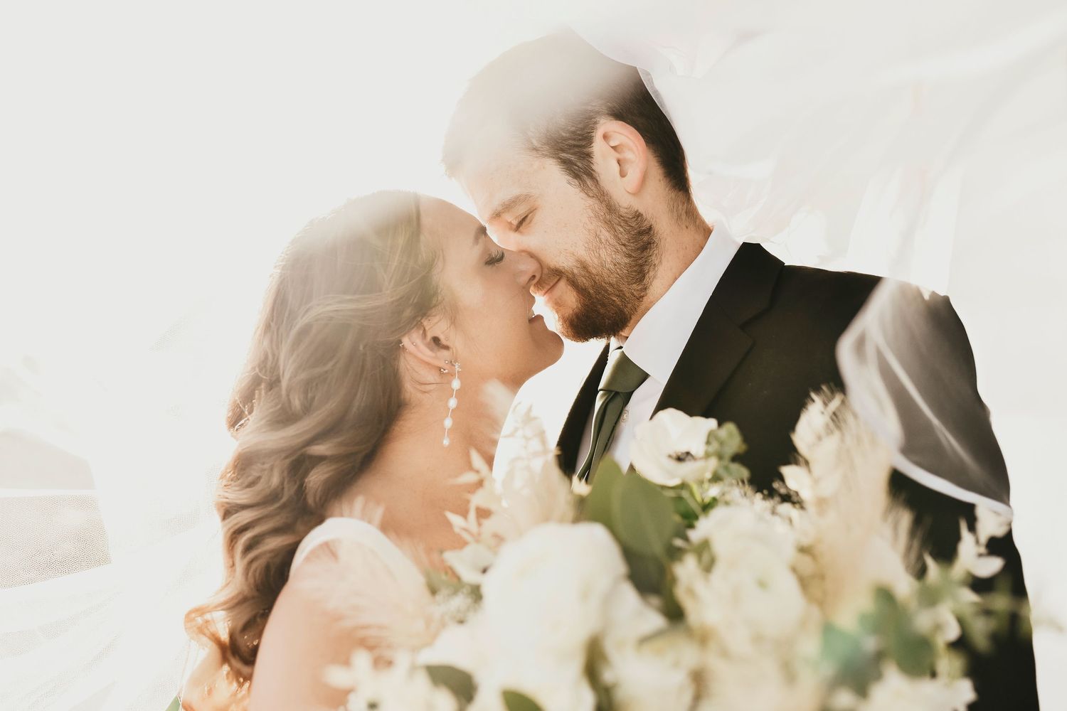 Golden hour light shining on bride and groom as they kiss under their veil in front of The Madelyn wedding venue