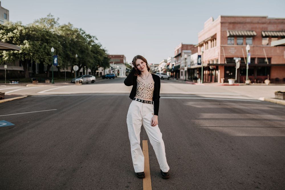 Person in cream colored pants and dark cardigan poses in the middle of an empty downtown street on a sunny day.