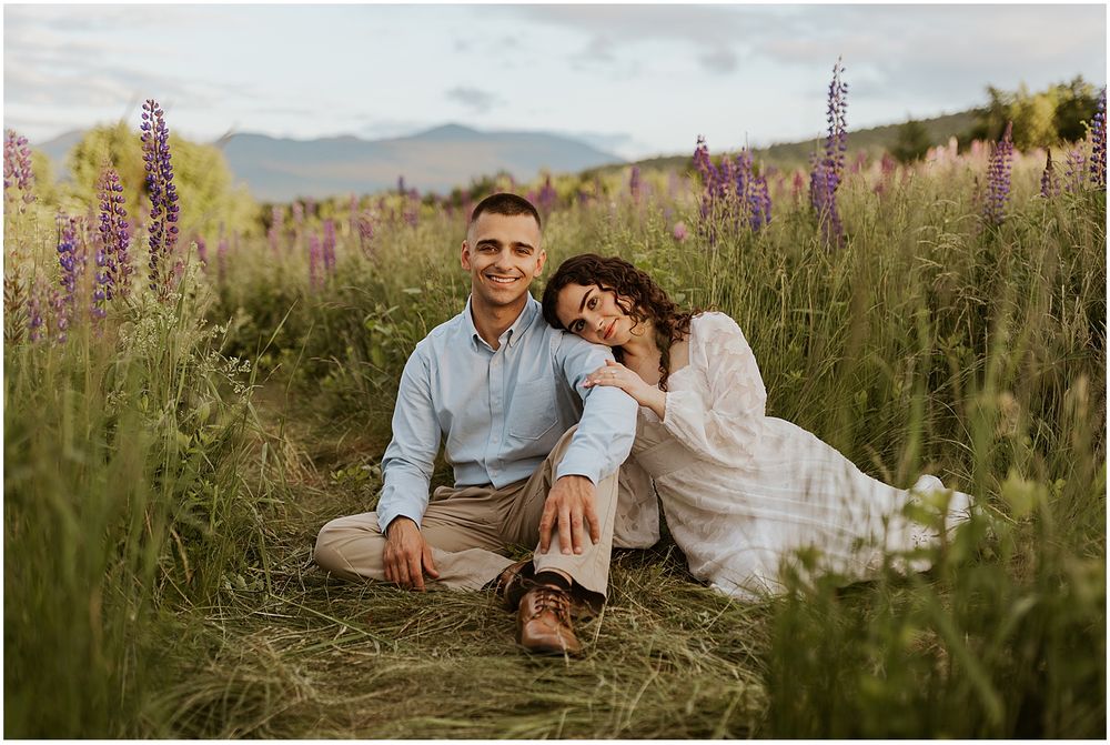 NH couple taking engagement pictures in a field of lupine flowers