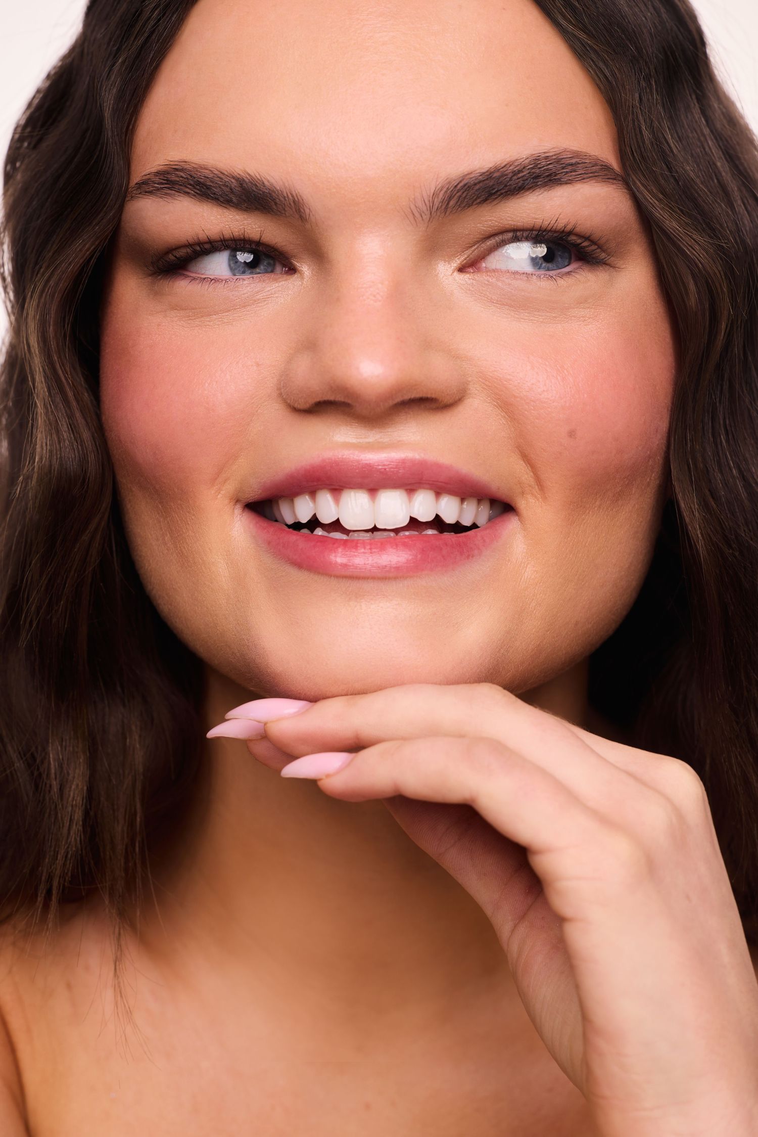 Close up beauty portrait showing bright white smile with wavy brown hair and natural glowing skin.