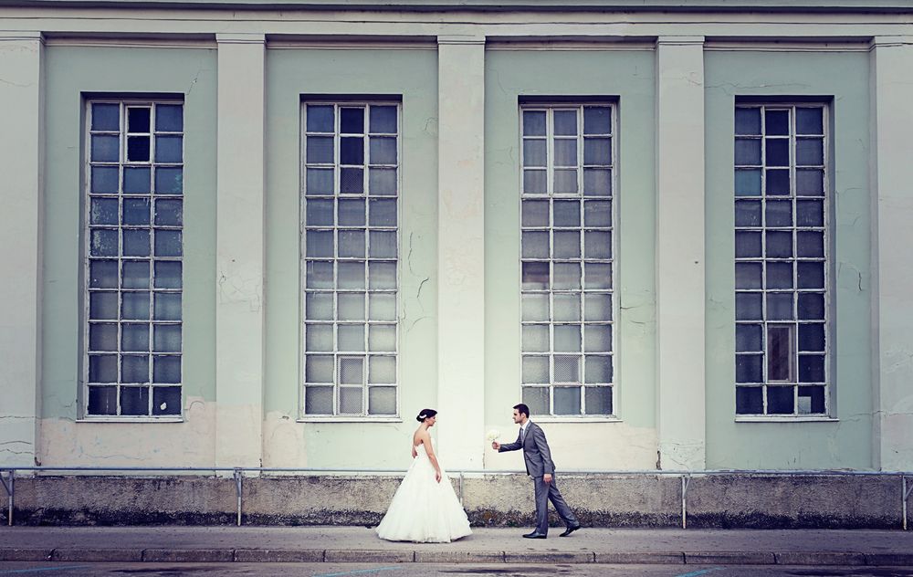 A bride and groom share a romantic moment against a wall with tall vintage windows.