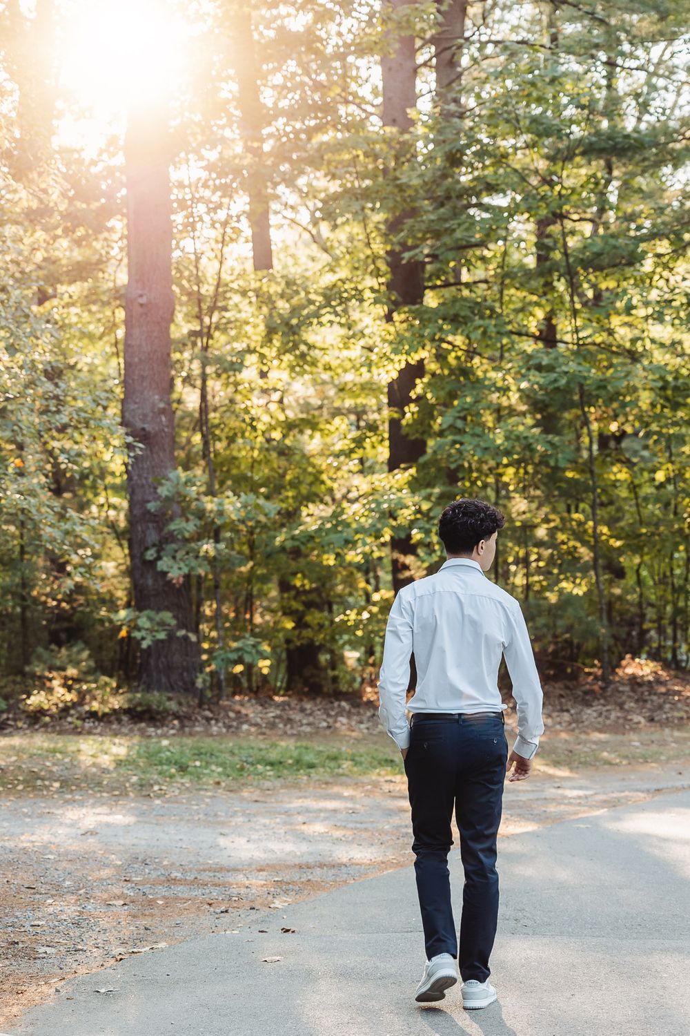 Person walking alone on a winding forest path during golden hour with sunlight filtering through autumn trees.
