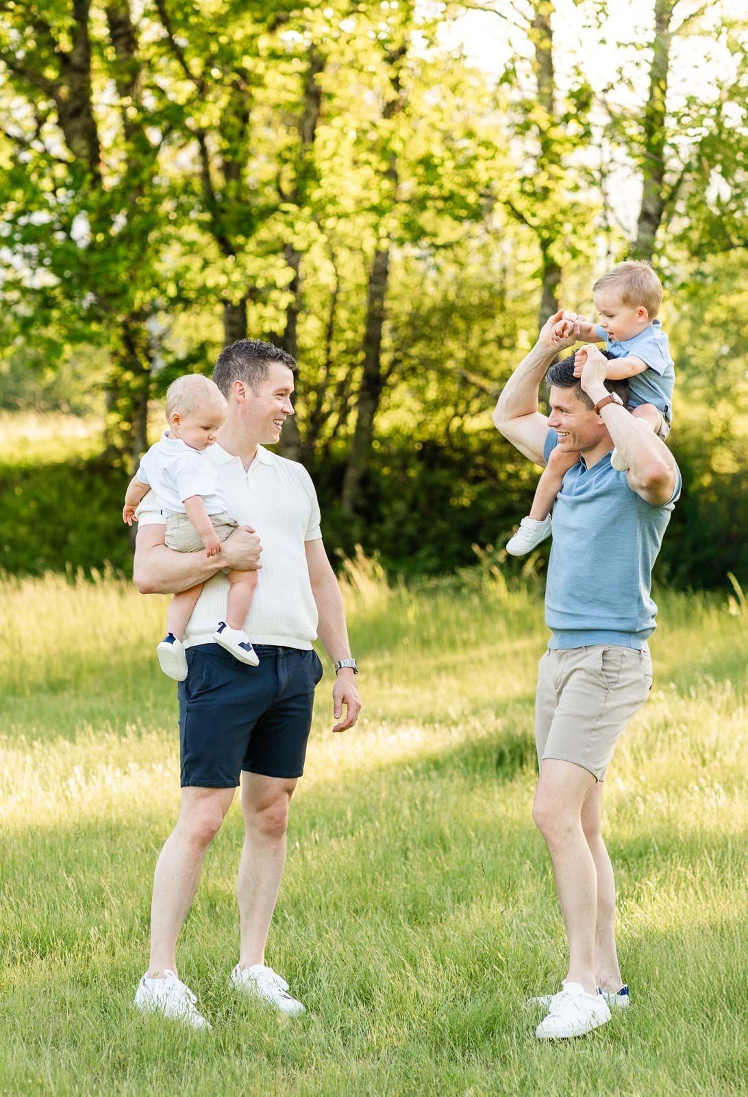Dads look at each other smiling while holding their children.