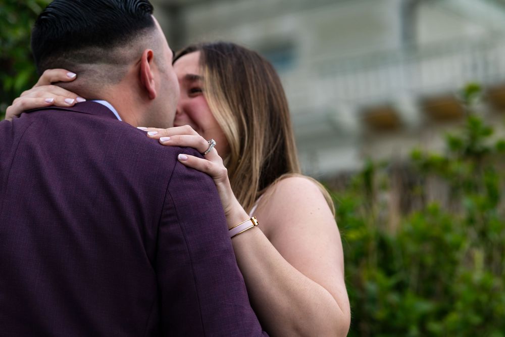 A romantic couple in formal attire share an intimate kiss in a garden setting during a wedding celebration.