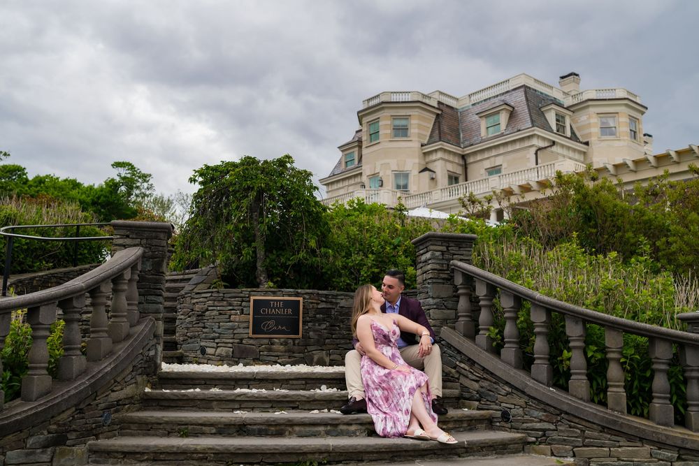 Romantic couple poses on a stone bridge surrounded by lush greenery and historic architecture.