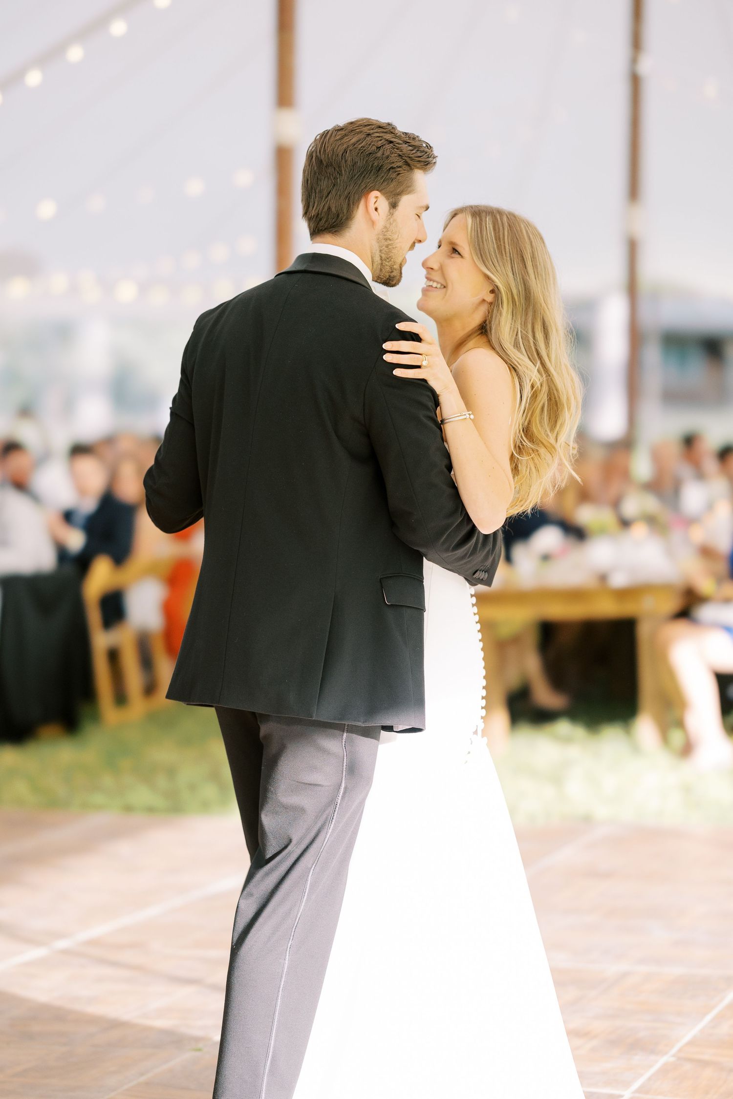 A couple shares an intimate first dance at their outdoor wedding reception under twinkling string lights.