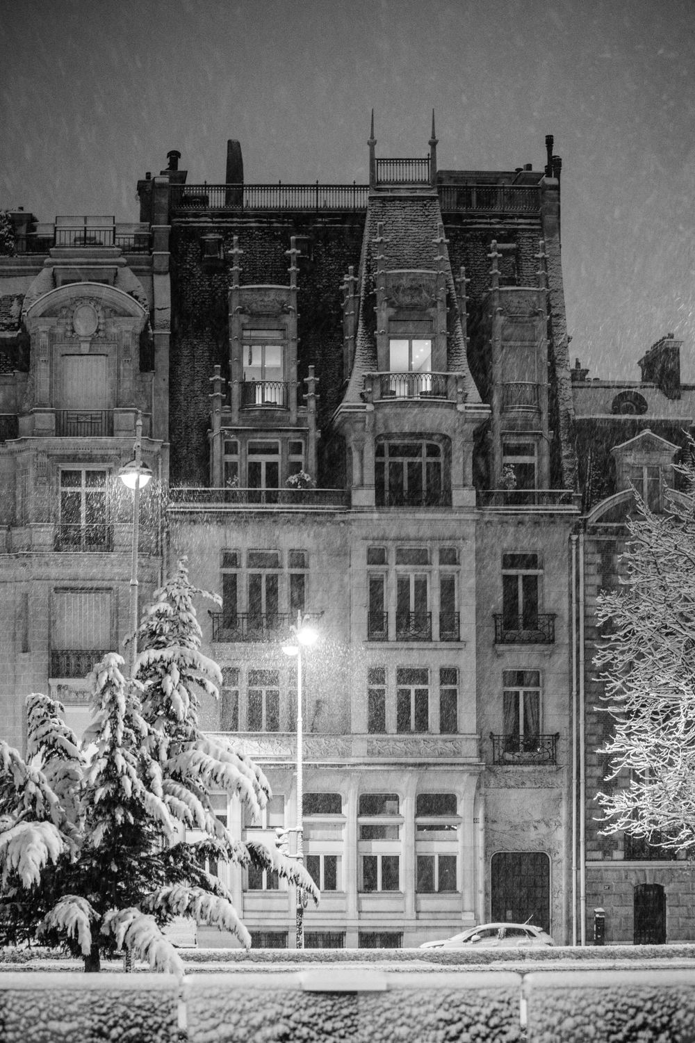 Snow-covered historic Parisian apartment building illuminated at night with ornate architectural details.