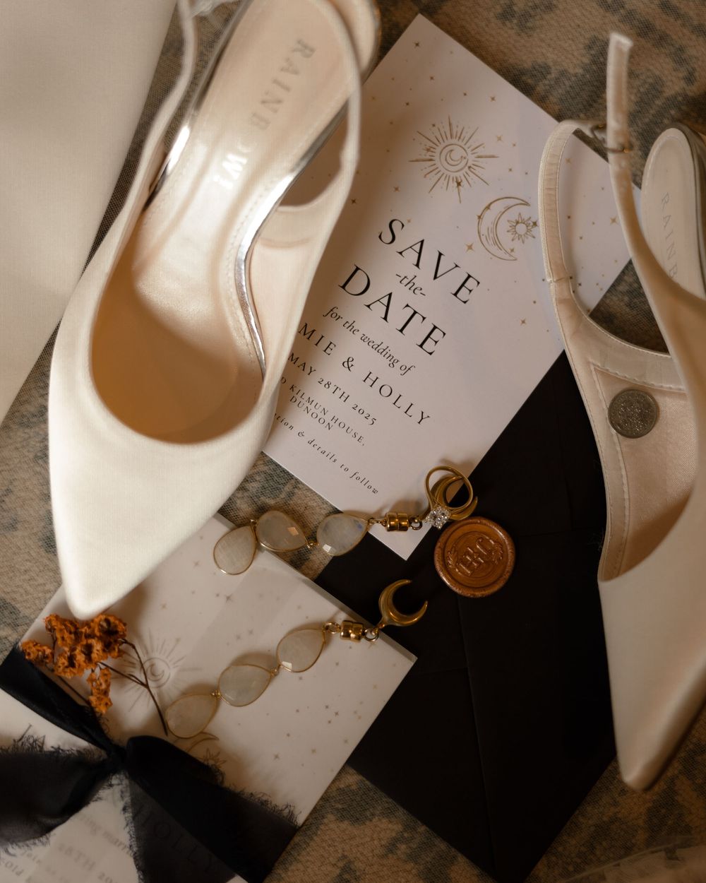 Elegant white bridal shoes next to a wedding save the date invitation with gold wax seal and decorative elements.