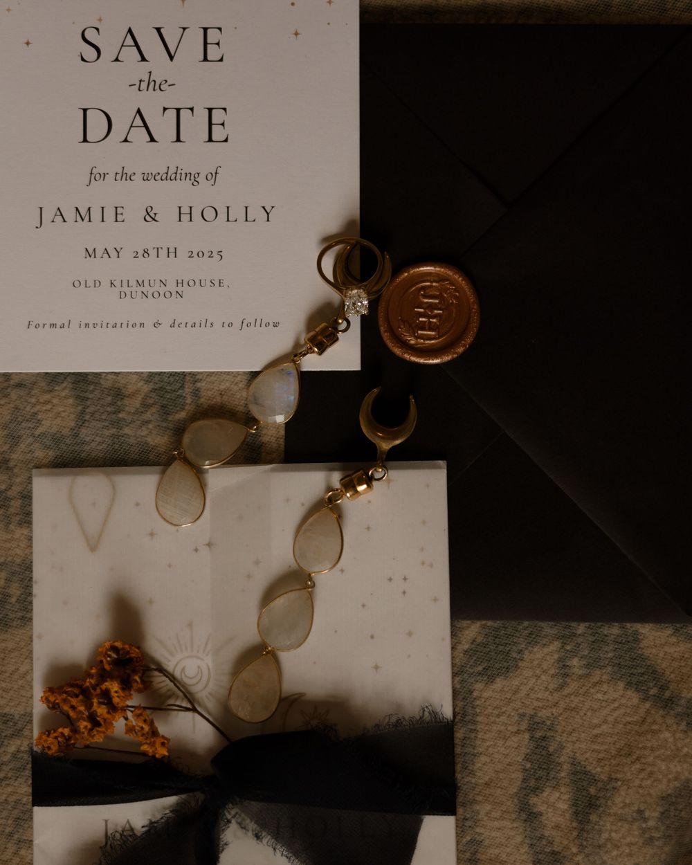 Wedding save the date card with wax seal and vintage jewelry details in moody lighting.