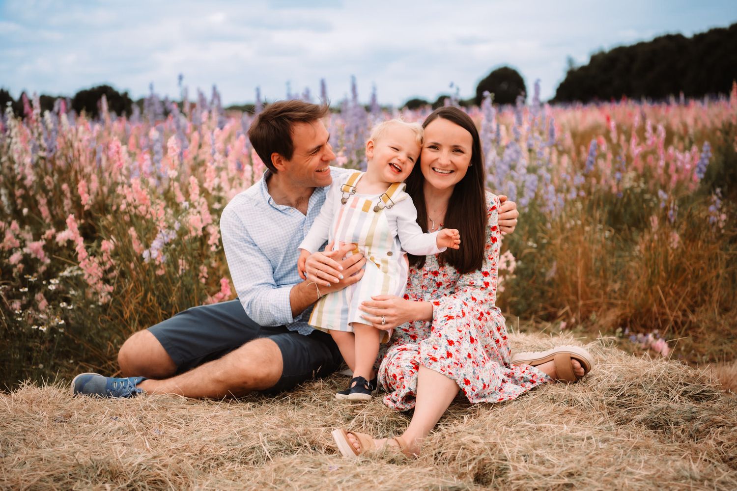 Family enjoying a sunny afternoon together in a field of pink wildflowers during golden hour.