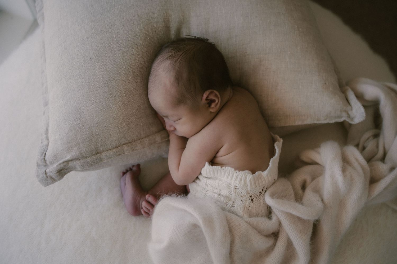 Newborn baby sleeping peacefully on white bedding against a grey pillow in Mansfield