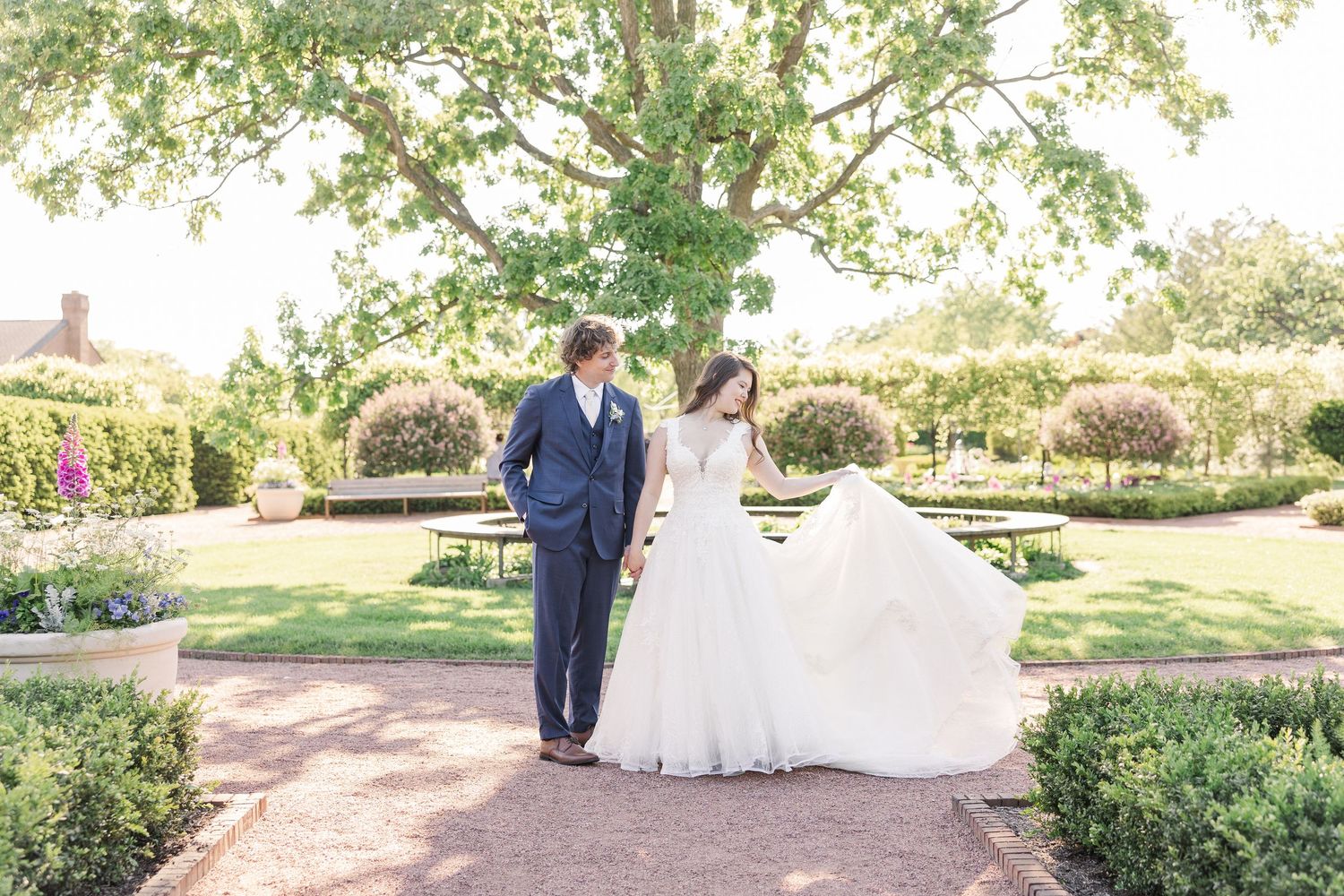 Beautiful wedding couple walking in a formal garden with bride's white dress flowing in majestic arch behind them.
