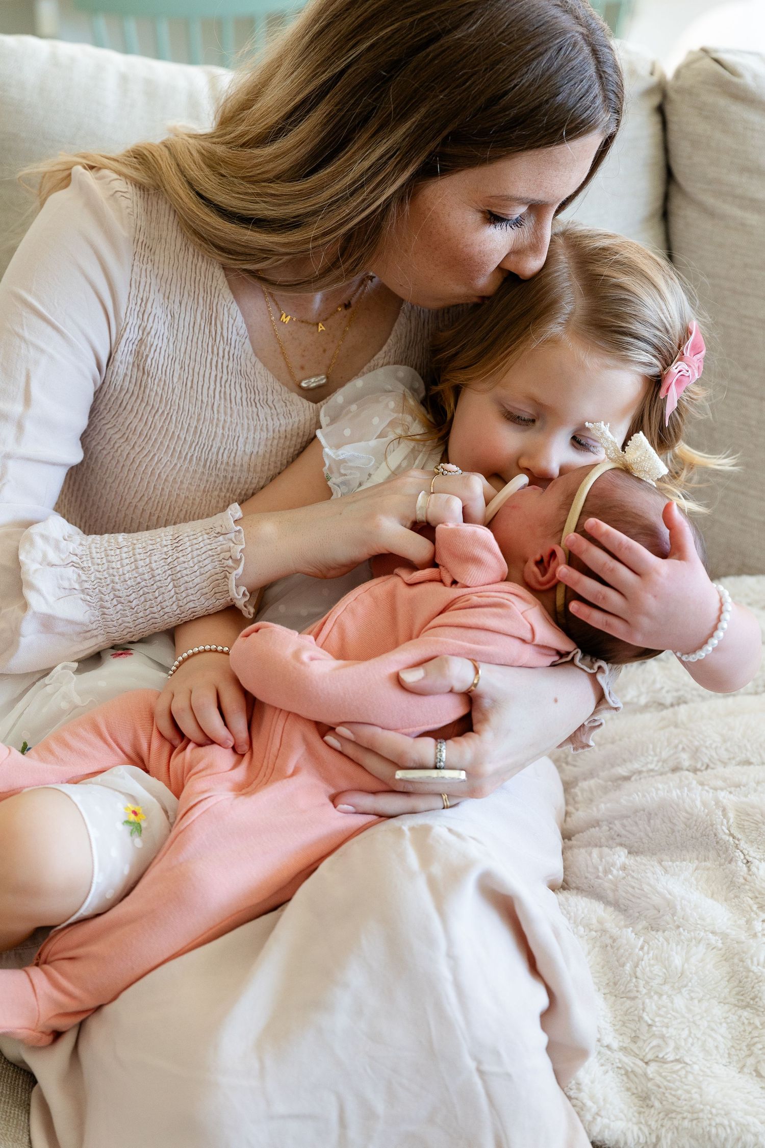 mom kissing top of toddlers head while holding toddler who is holding newborn. toddler kissing newborn.