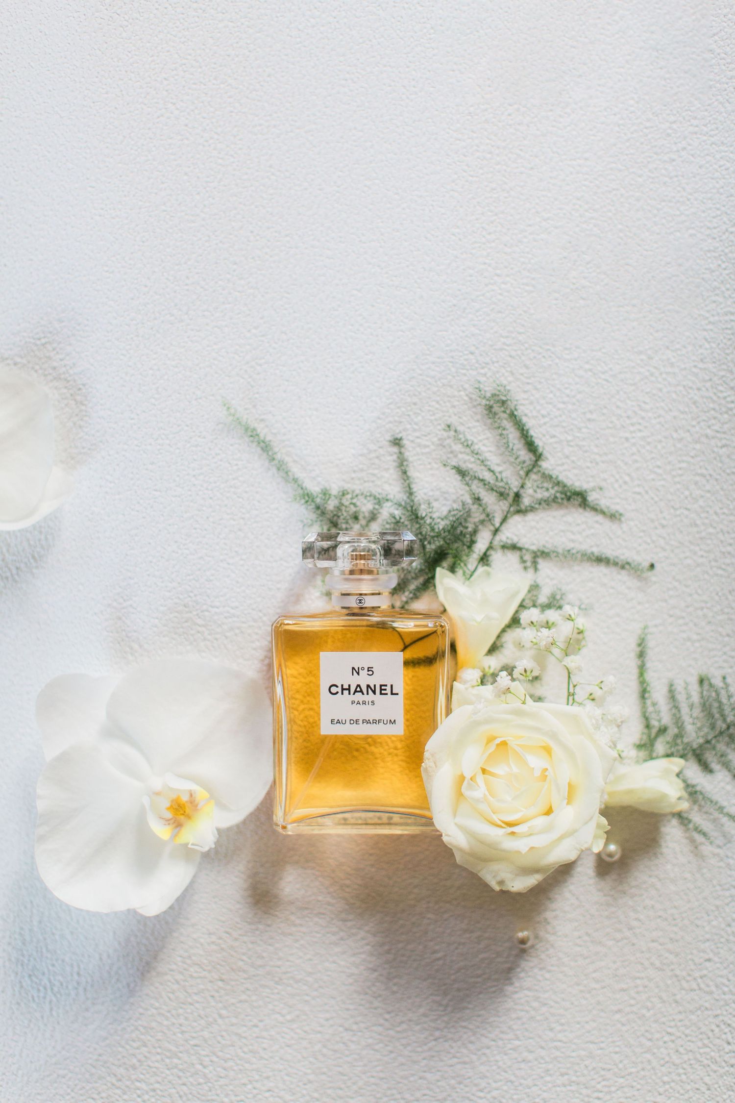 Elegant flatlay of Chanel No 5 perfume with delicate white roses and orchids on a light backdrop by Hayley Elizabeth photography cotswolds