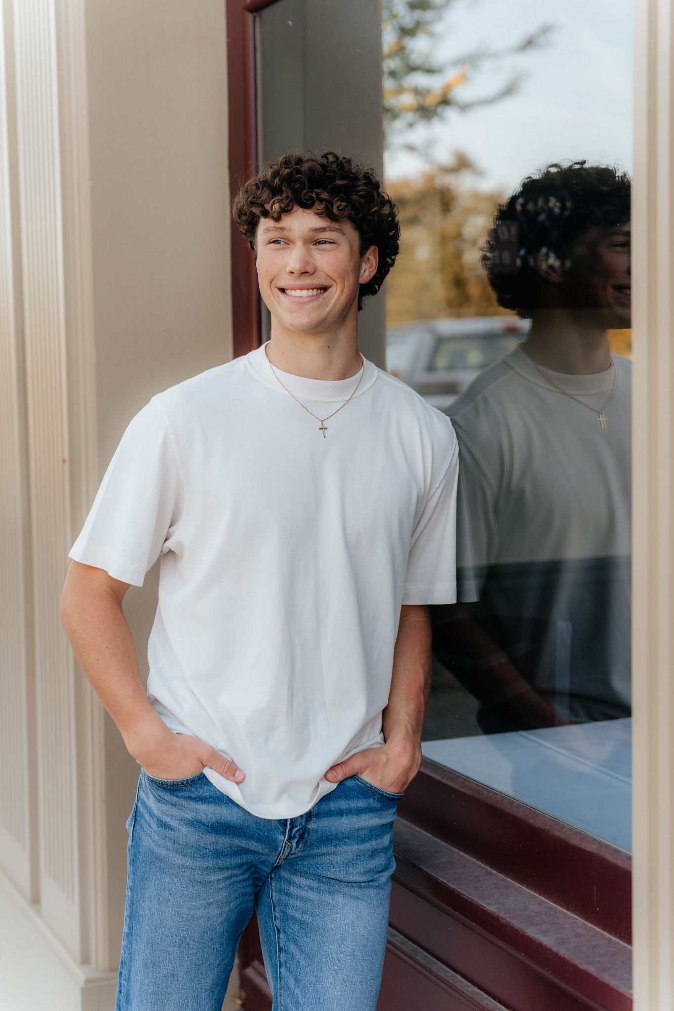 A casual portrait against a window reflection wearing a white t-shirt and blue jeans.