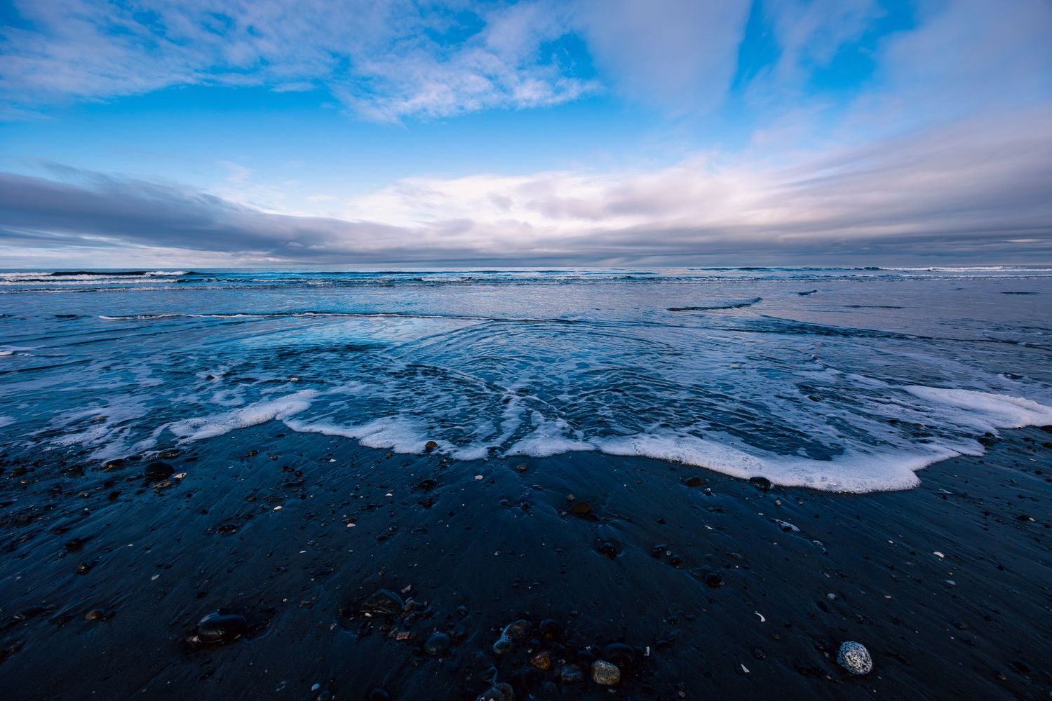 Dramatic blue ocean waves crash on a rocky beach under cloudy skies at dusk on North Beach, Haida Gwaii.