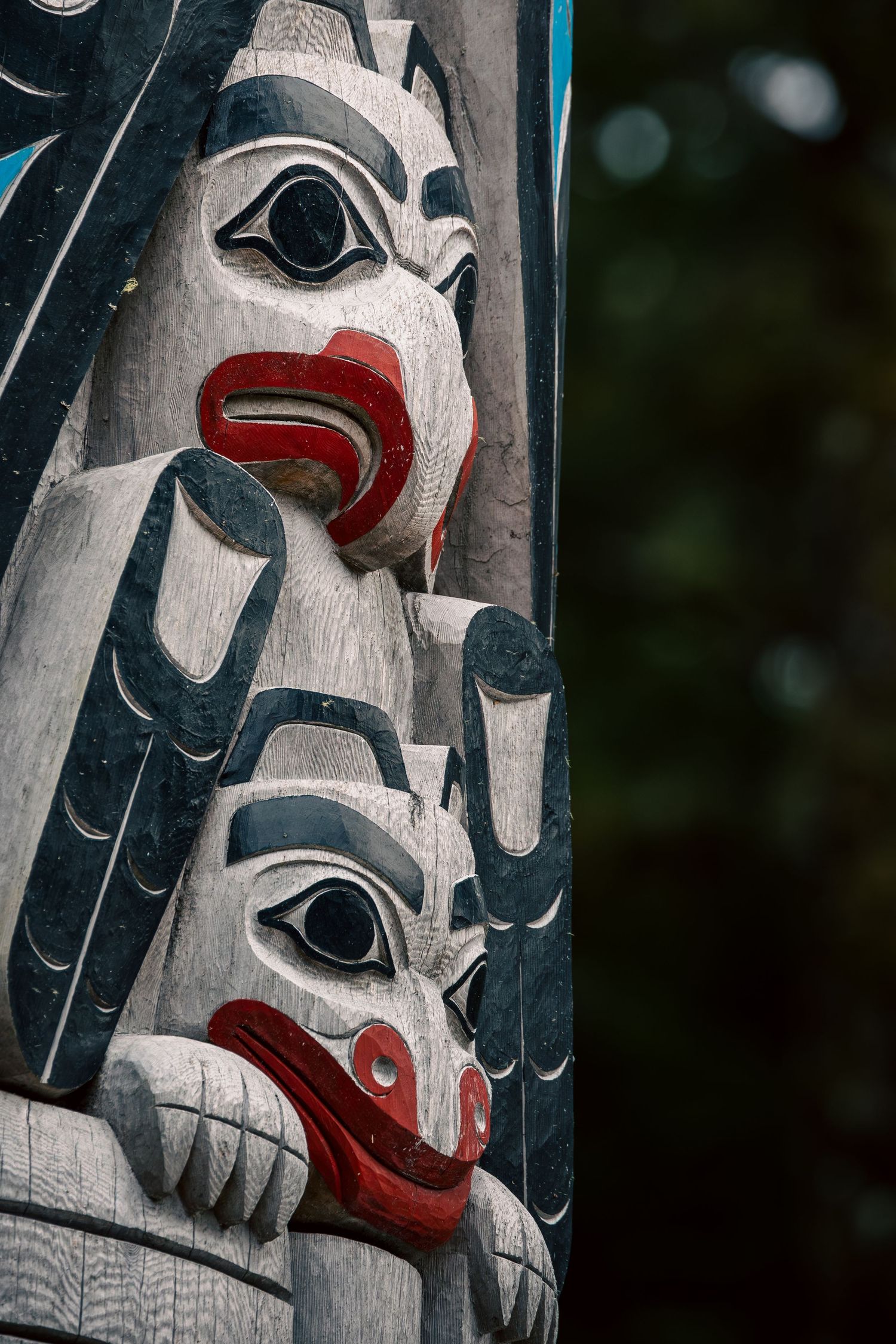 Traditional Haida totem pole faces with black, red and white paint details.