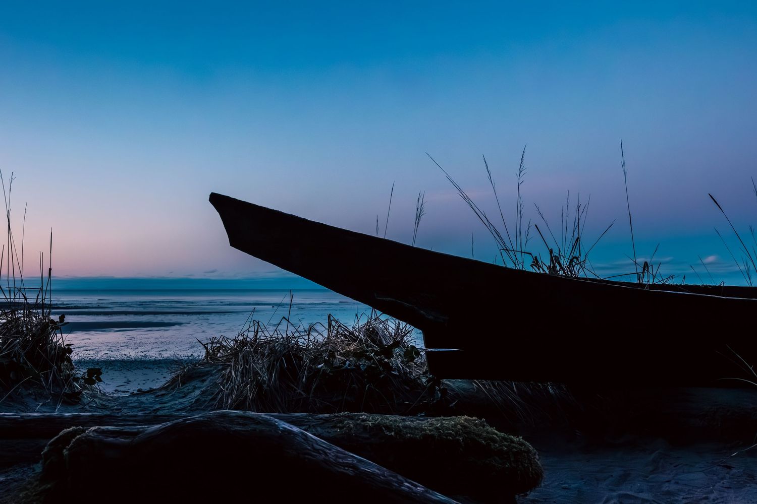 Silhouette of a Haida canoe against twilight sky with ocean backdrop and beach grass in foreground located at wedding beach on Haida Gwaii.
