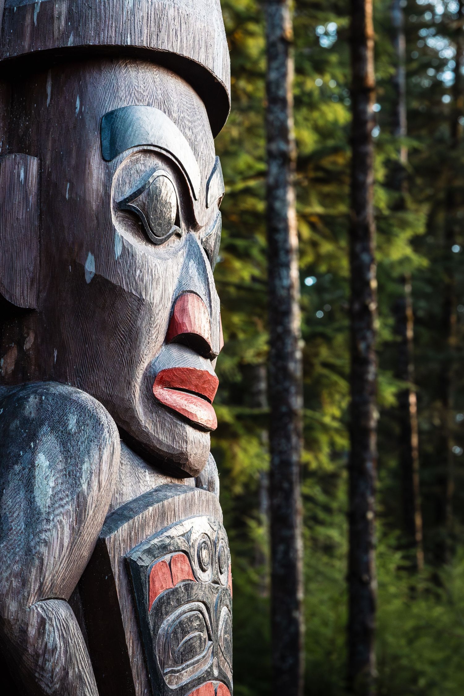Detailed view of a Haida totem pole carving with vibrant colours against a forested background.