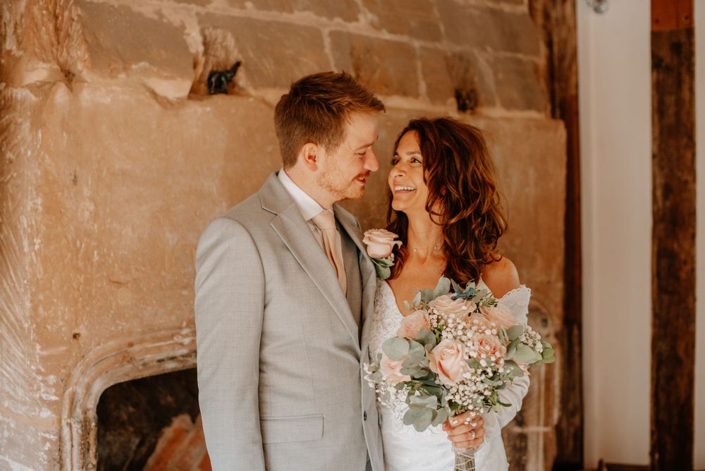 A romantic wedding couple in rustic setting with groom in light gray suit and bride holding pastel bouquet.