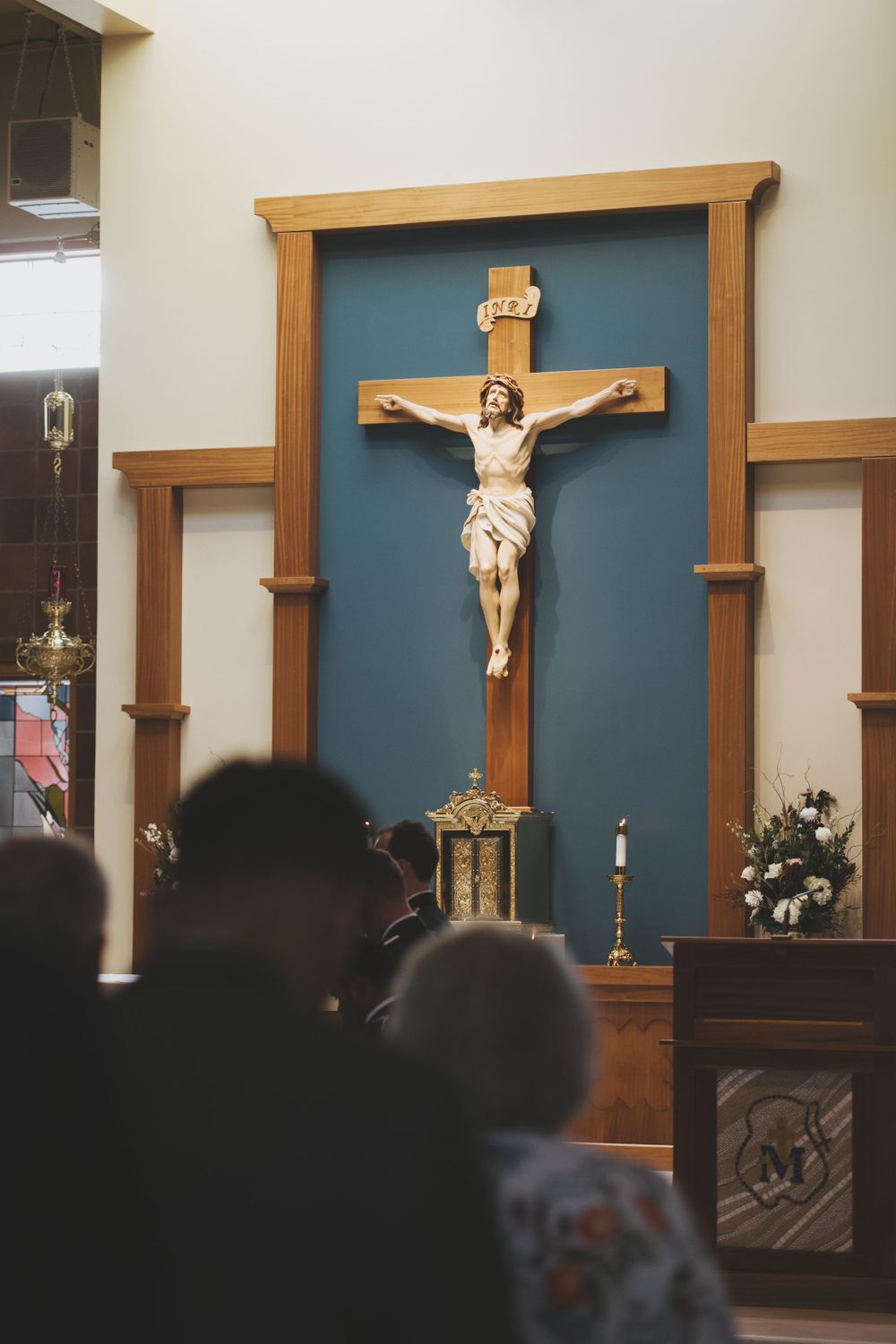 Wooden crucifix mounted on blue wall in church interior with silhouettes of people in foreground.