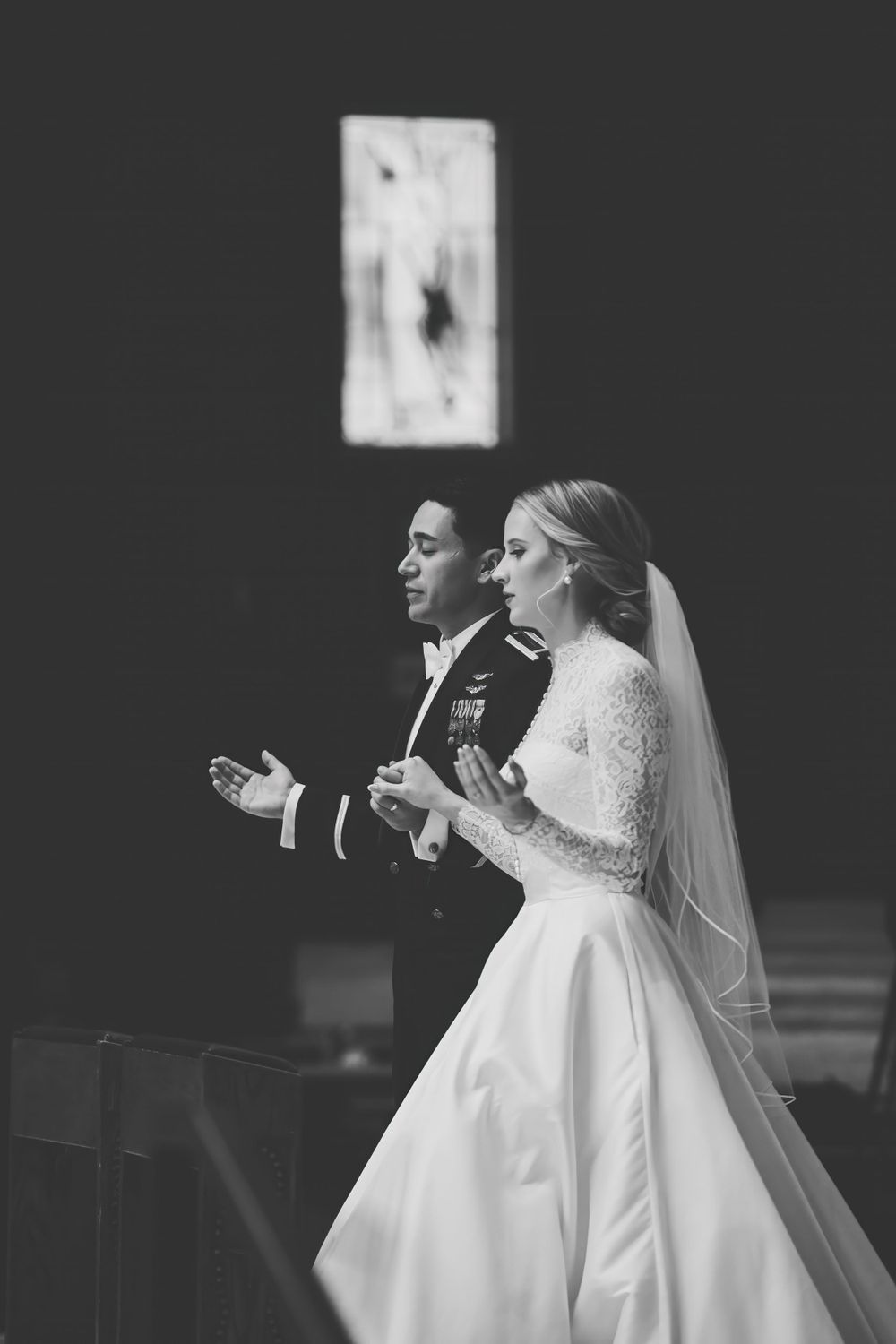 A black and white wedding photo showing a couple singing together during their ceremony, with the bride wearing a veil and lace gown.