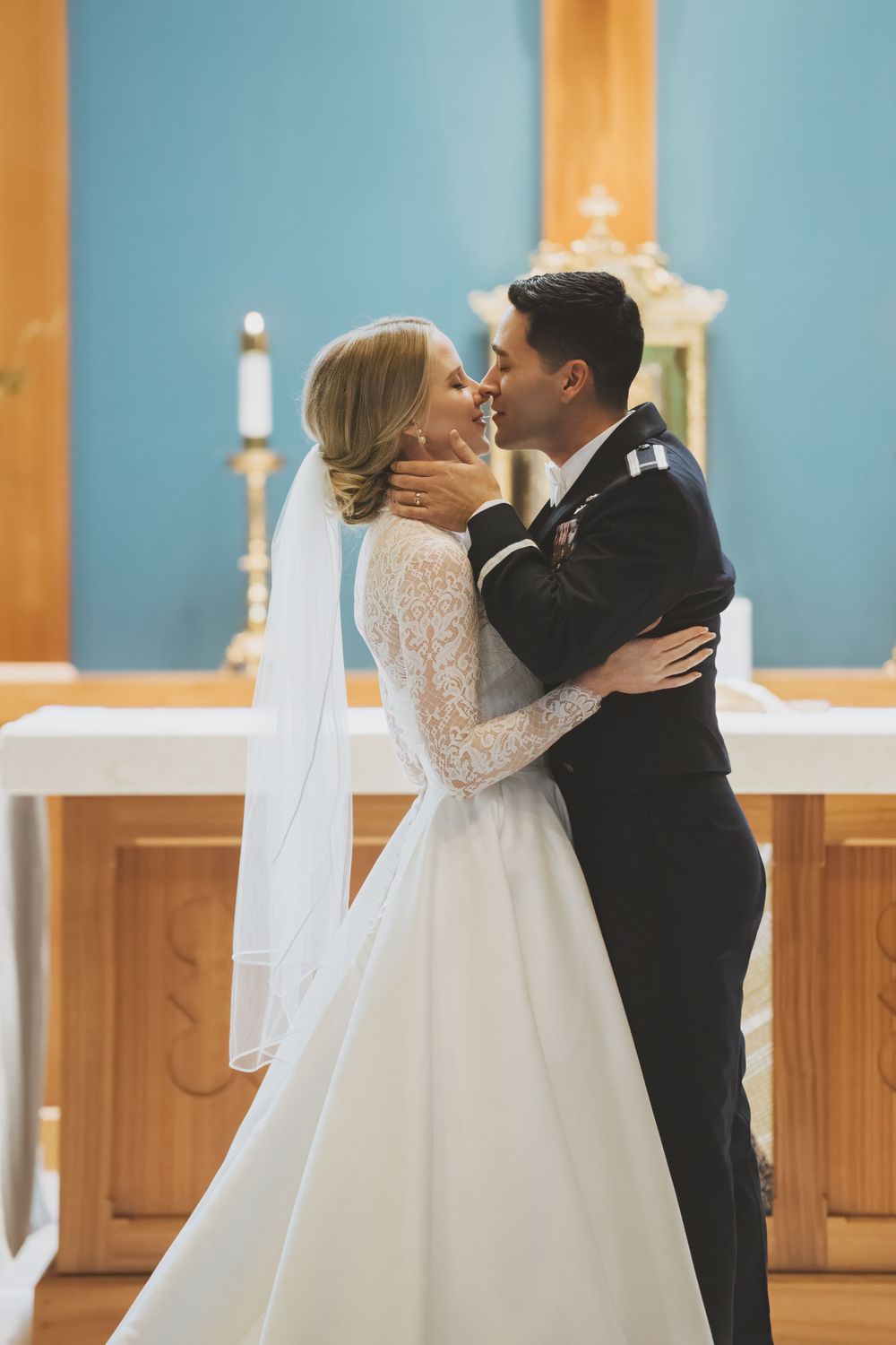 A romantic wedding moment captured in a church with the couple embracing in front of a blue wall and altar.