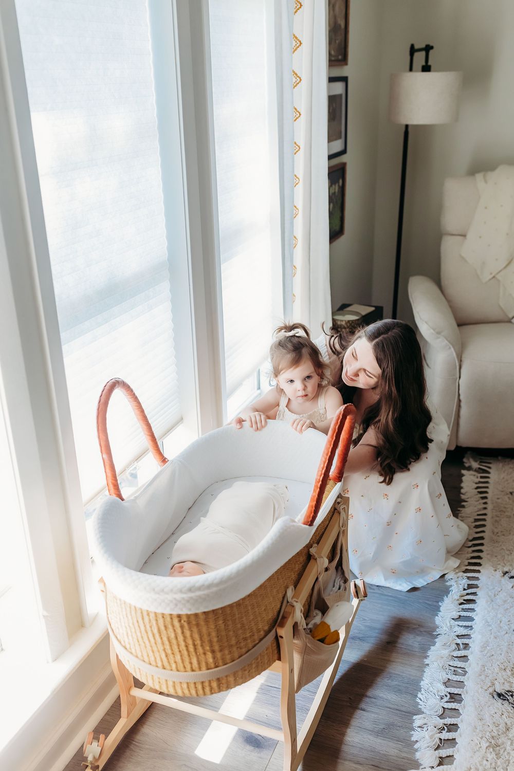 A nursery corner with a woven bassinet stand by a bright window with someone looking over the crib.
