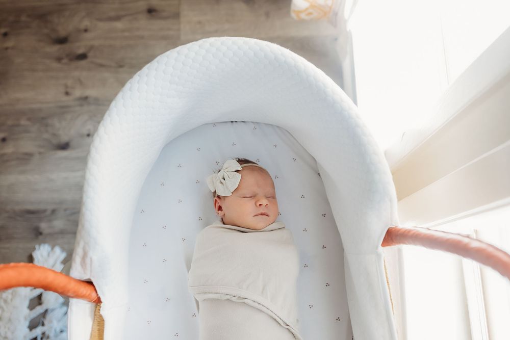 A tiny baby sleeps cozy and swaddled in a white upholstered rocking chair near a rustic wooden wall.