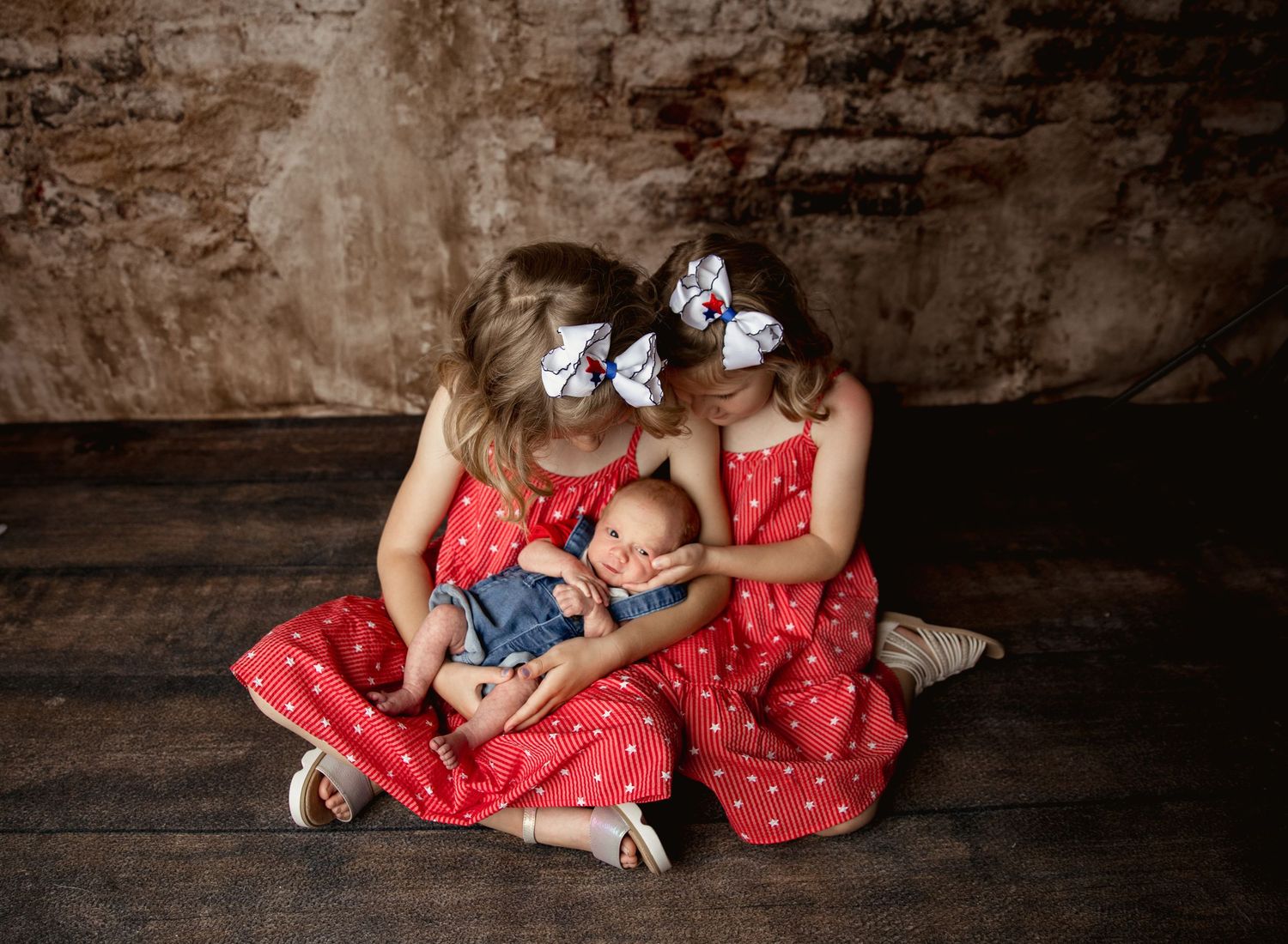 Mother and baby wearing matching red dresses lie together on rustic wooden floor during photoshoot.