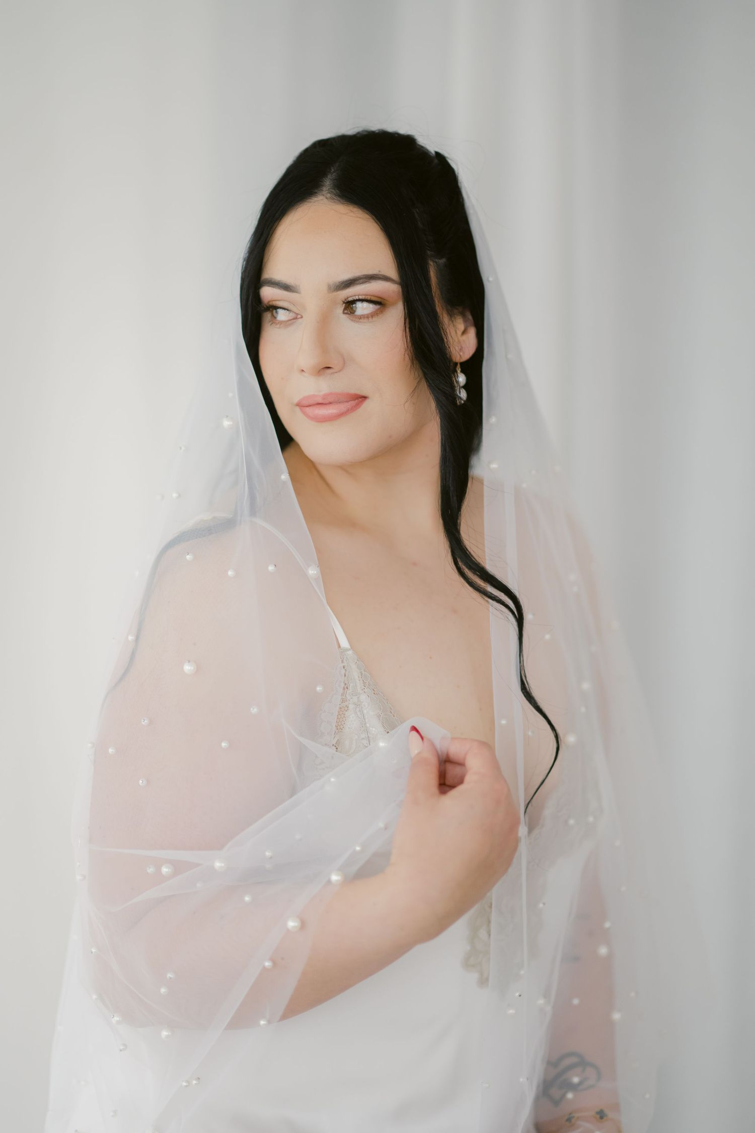 Bride in traditional white bridal attire gazes sideways while wearing long flowy veil with delicate sparkly details.