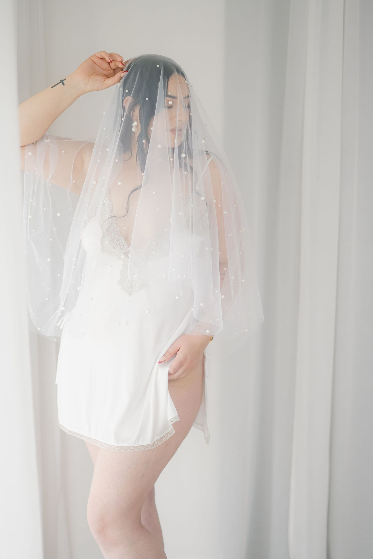 Ethereal bridal boudoir photo with soft white veil and robe in natural window light.