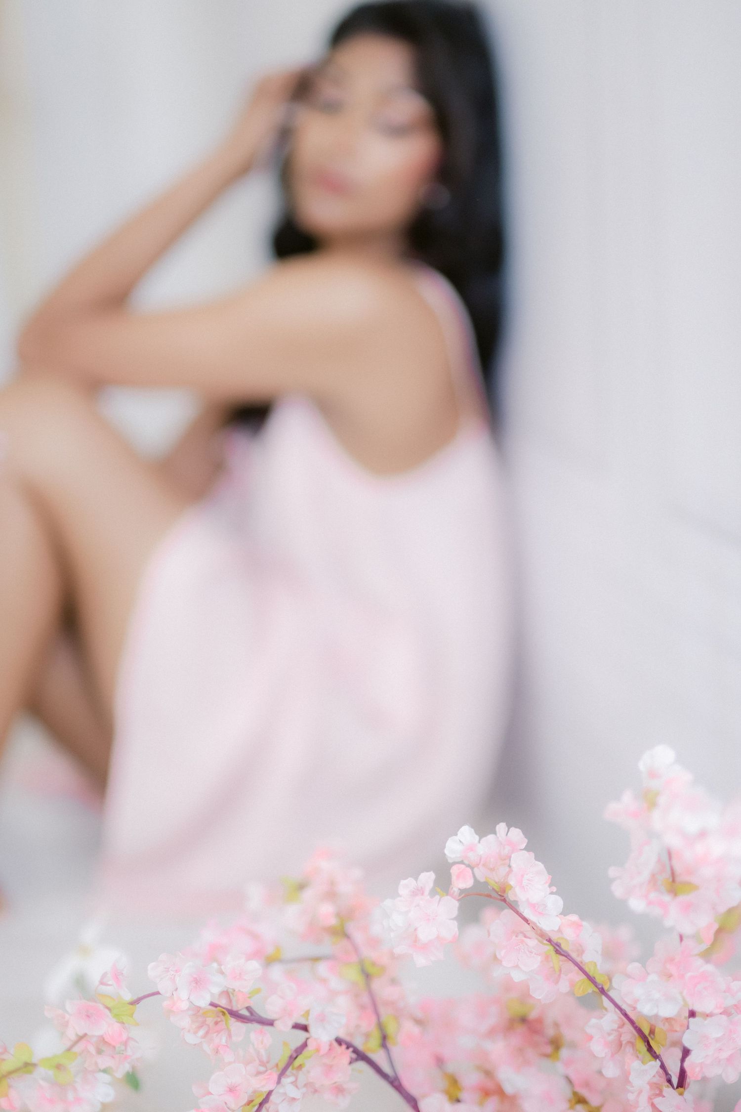 Dreamy soft-focus portrait with cherry blossoms in foreground creating romantic spring atmosphere.