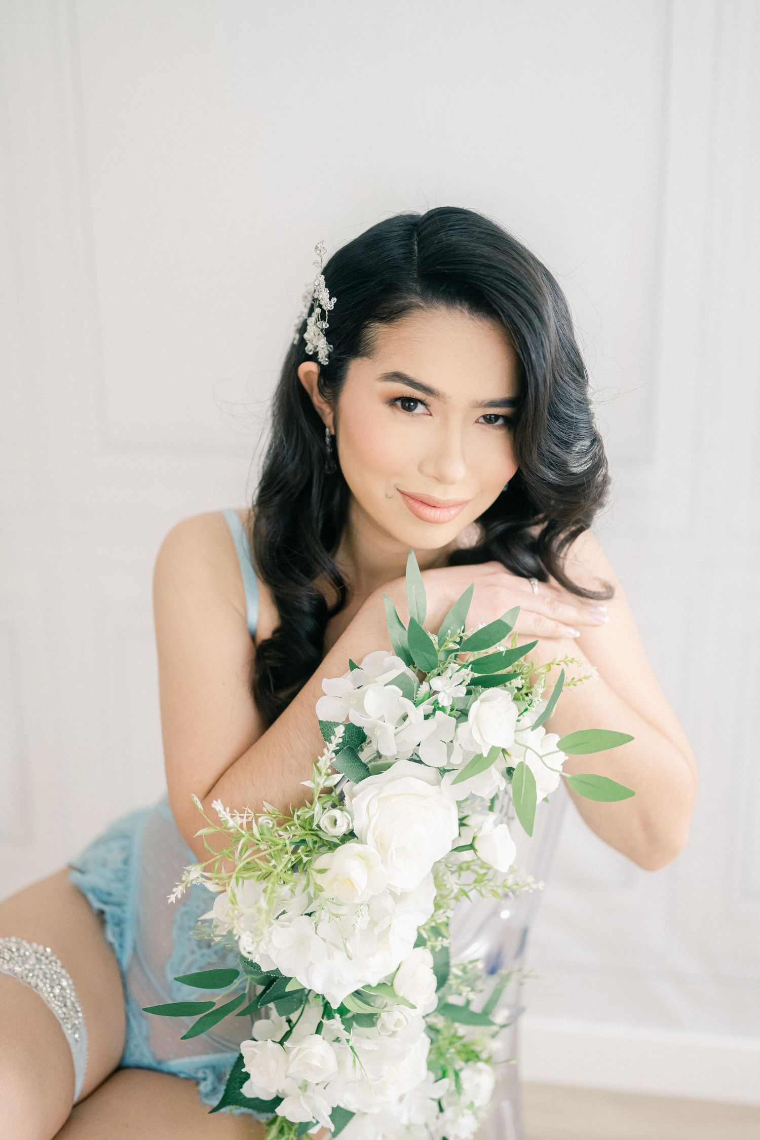 A bridal portrait with luxurious white flowers and greenery bouquet against a light backdrop.