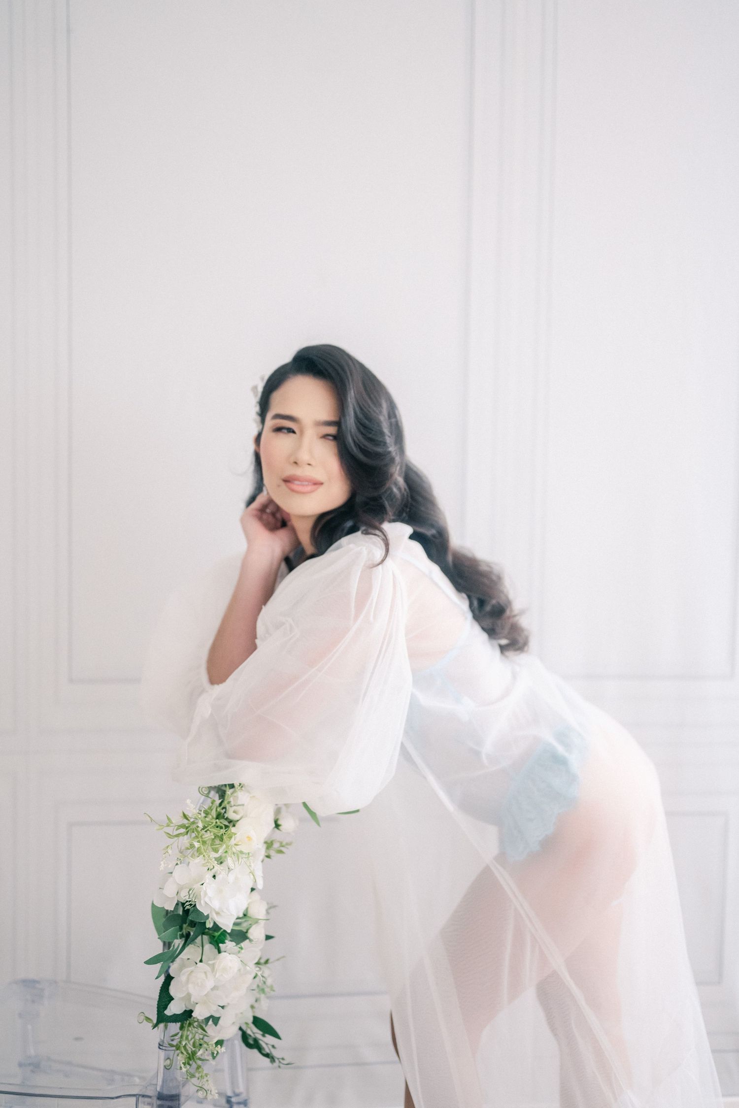 Ethereal boudoir photography with flowing white robe and soft blue lingerie against classic white wall panels.