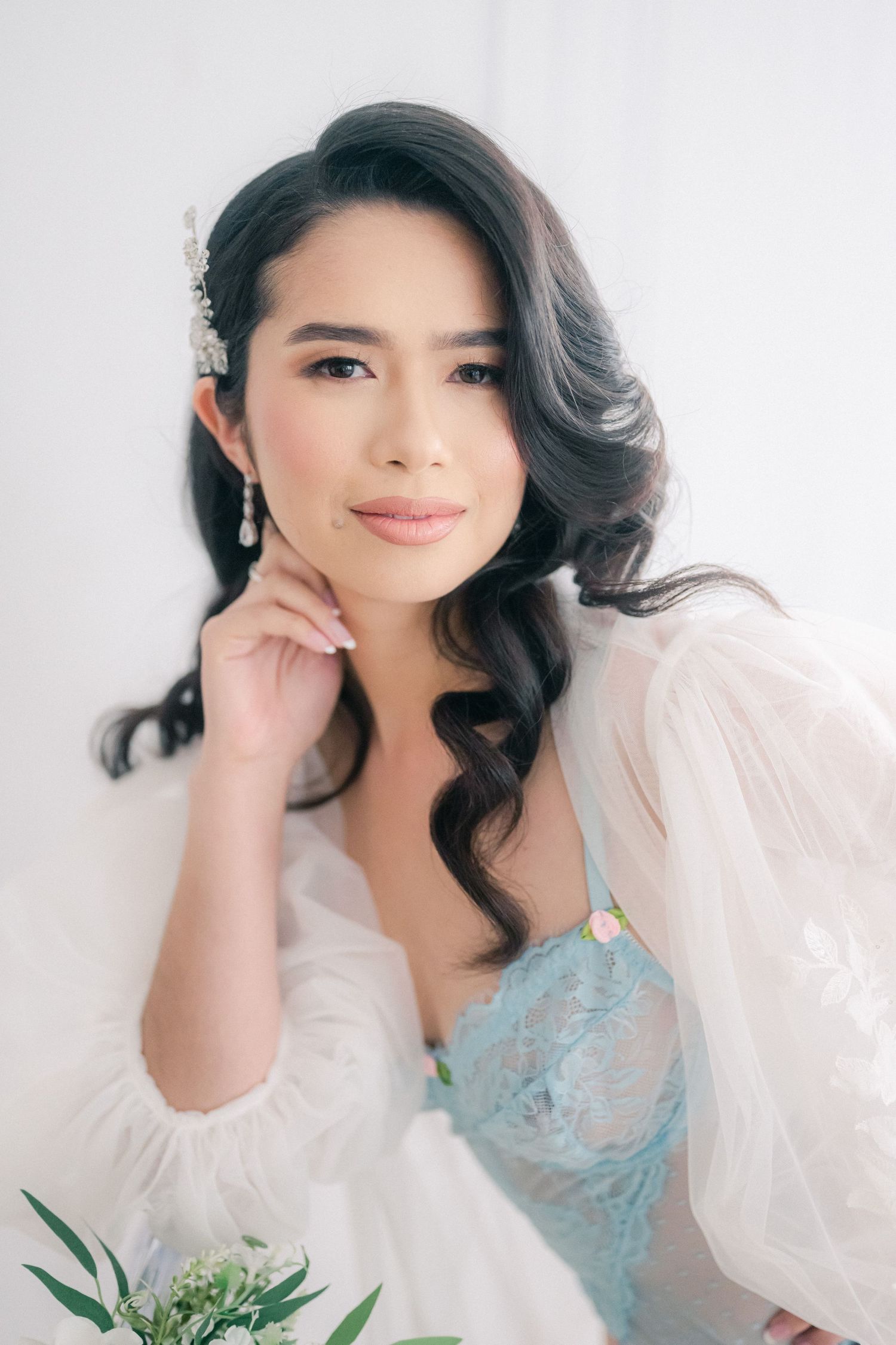 Portrait with soft white sheer sleeves and ethereal blue dress against white background, holding greenery.