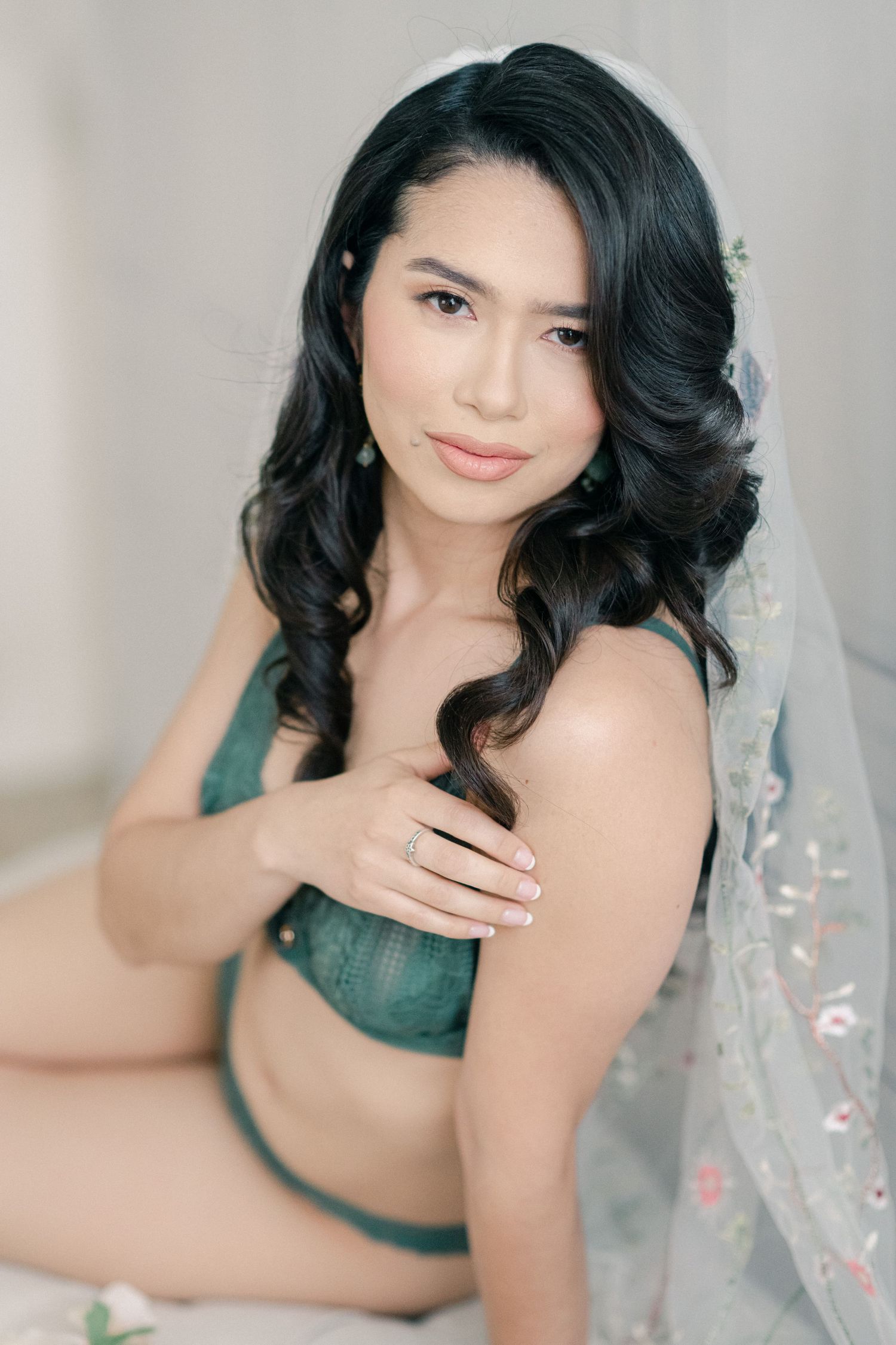Elegant boudoir portrait with romantic styling, dark wavy hair and delicate veil details.
