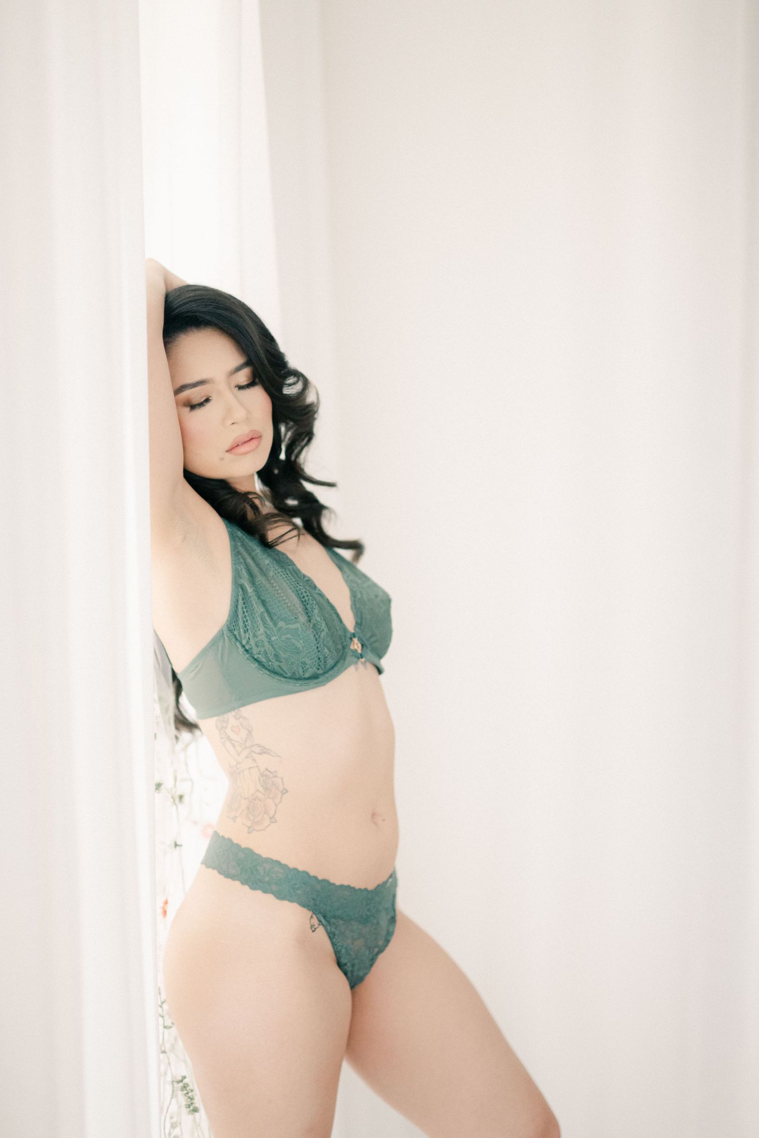 Sensual boudoir photo against white curtains featuring emerald green lingerie set.
