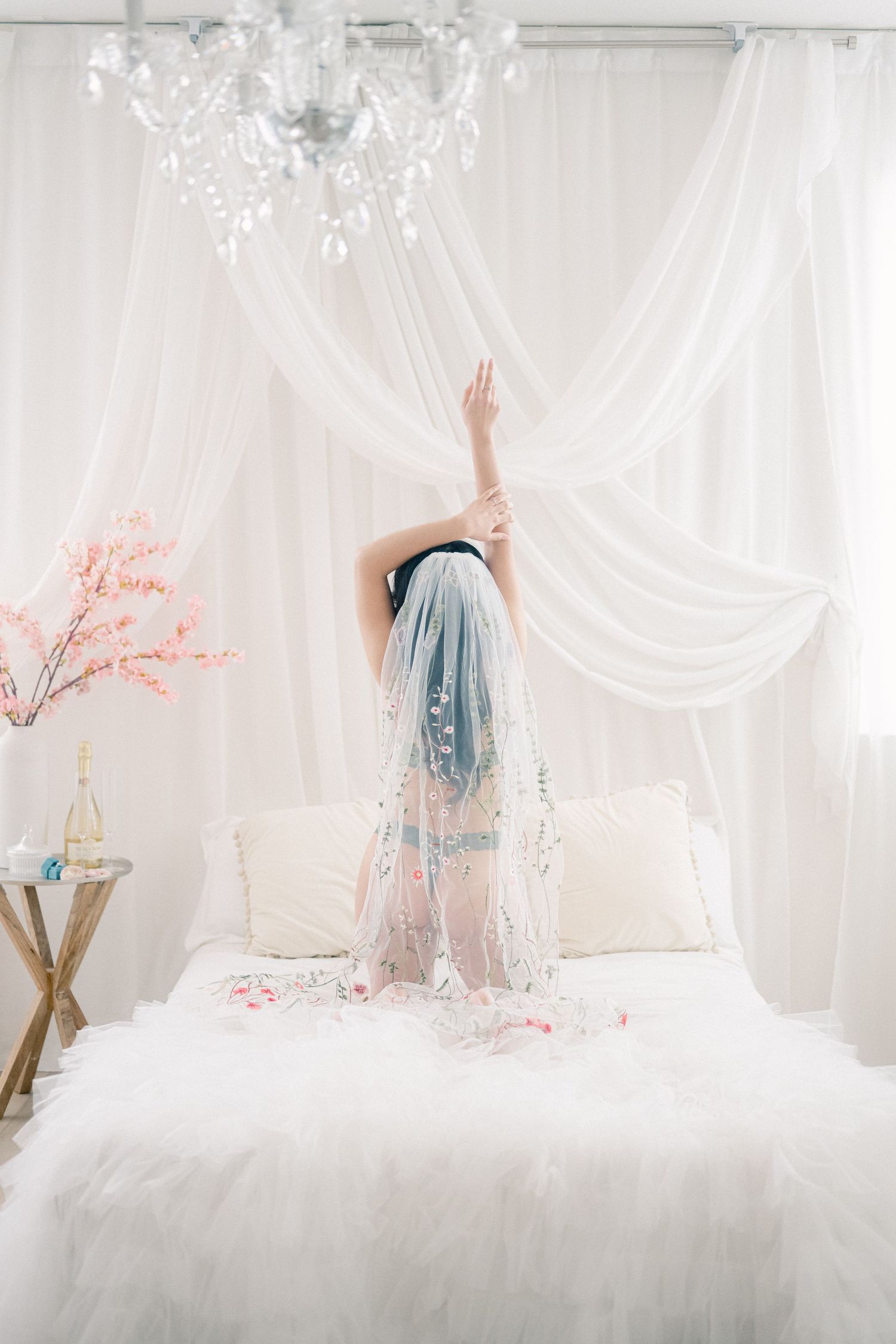 Ethereal bedroom scene with crystal chandelier, flowing white curtains, and blue-haired figure on white bedding.