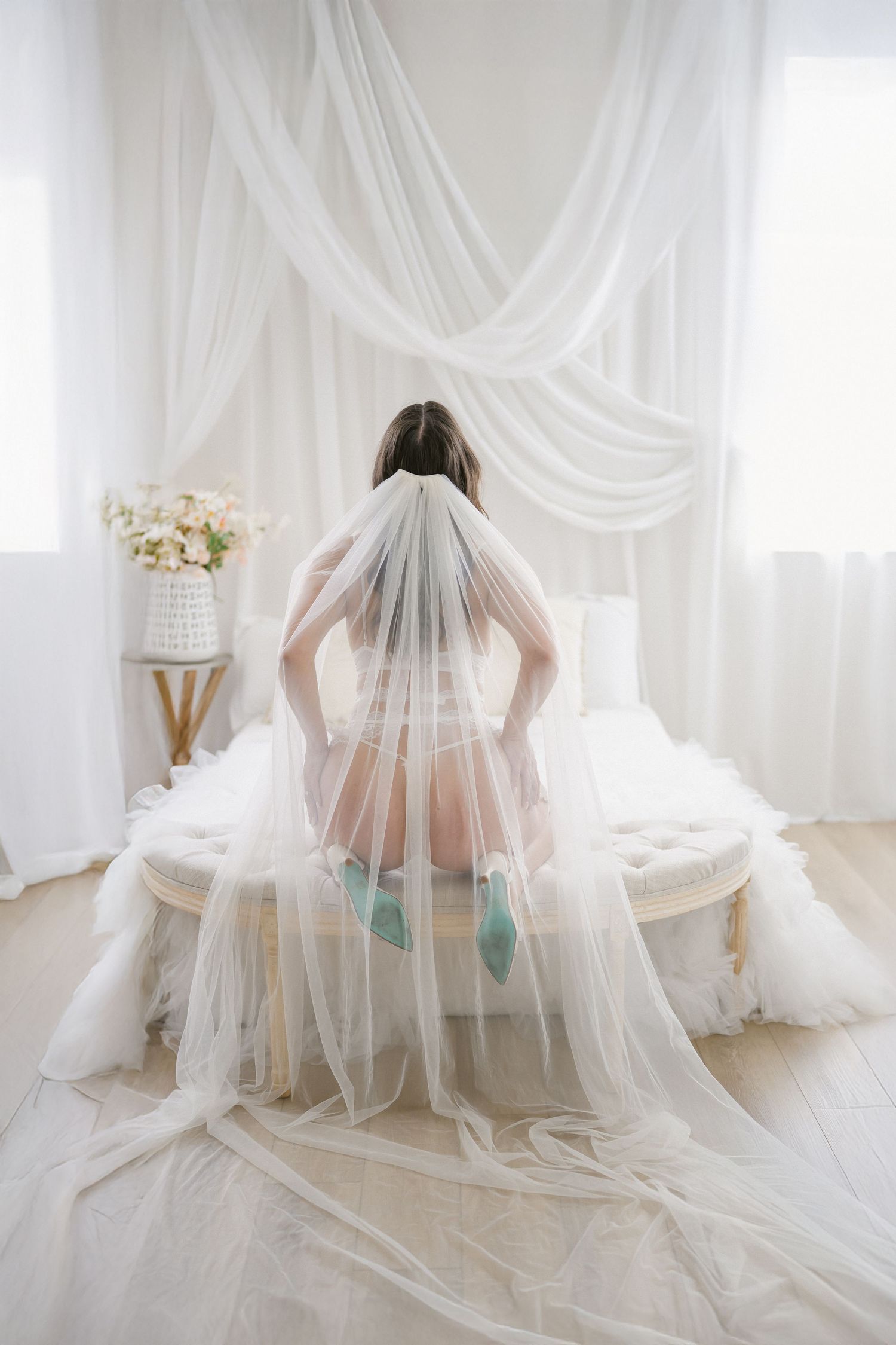 Ethereal bridal boudoir photo with flowing white tulle veil and mint blue details in a light-filled studio setting.